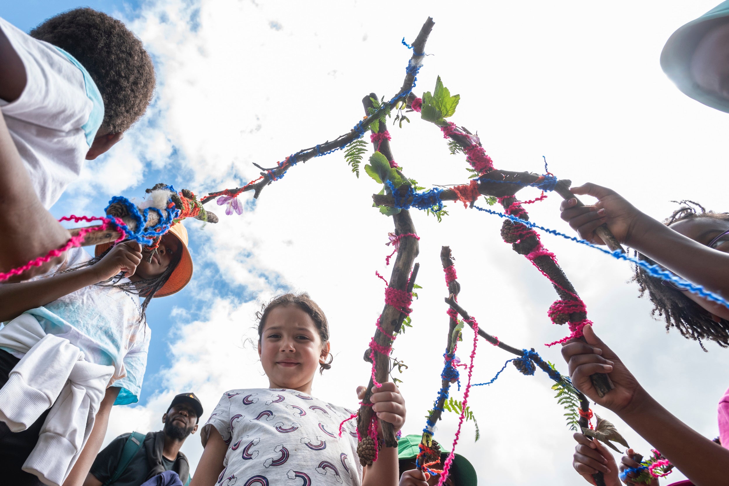 A group of children stood in a circle holding sticks decorated in things they've found in nature