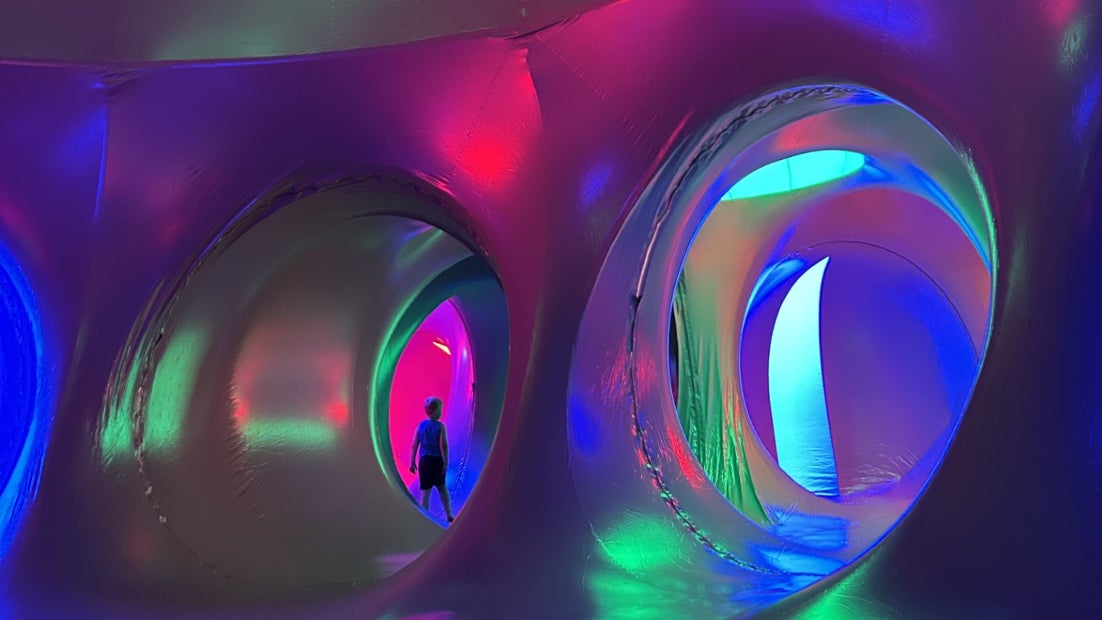 Image of a person walking in a huge walk in colourful inflatable sculpture featuring numerous tunnels and domes