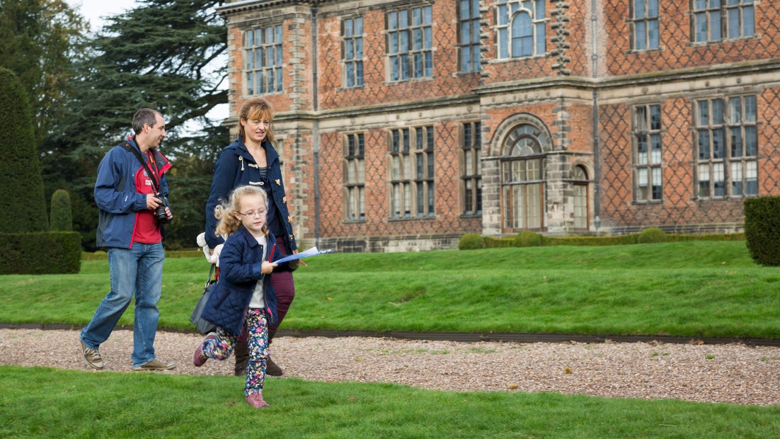 A family walking across the garden terraces during autumn with the house in the background