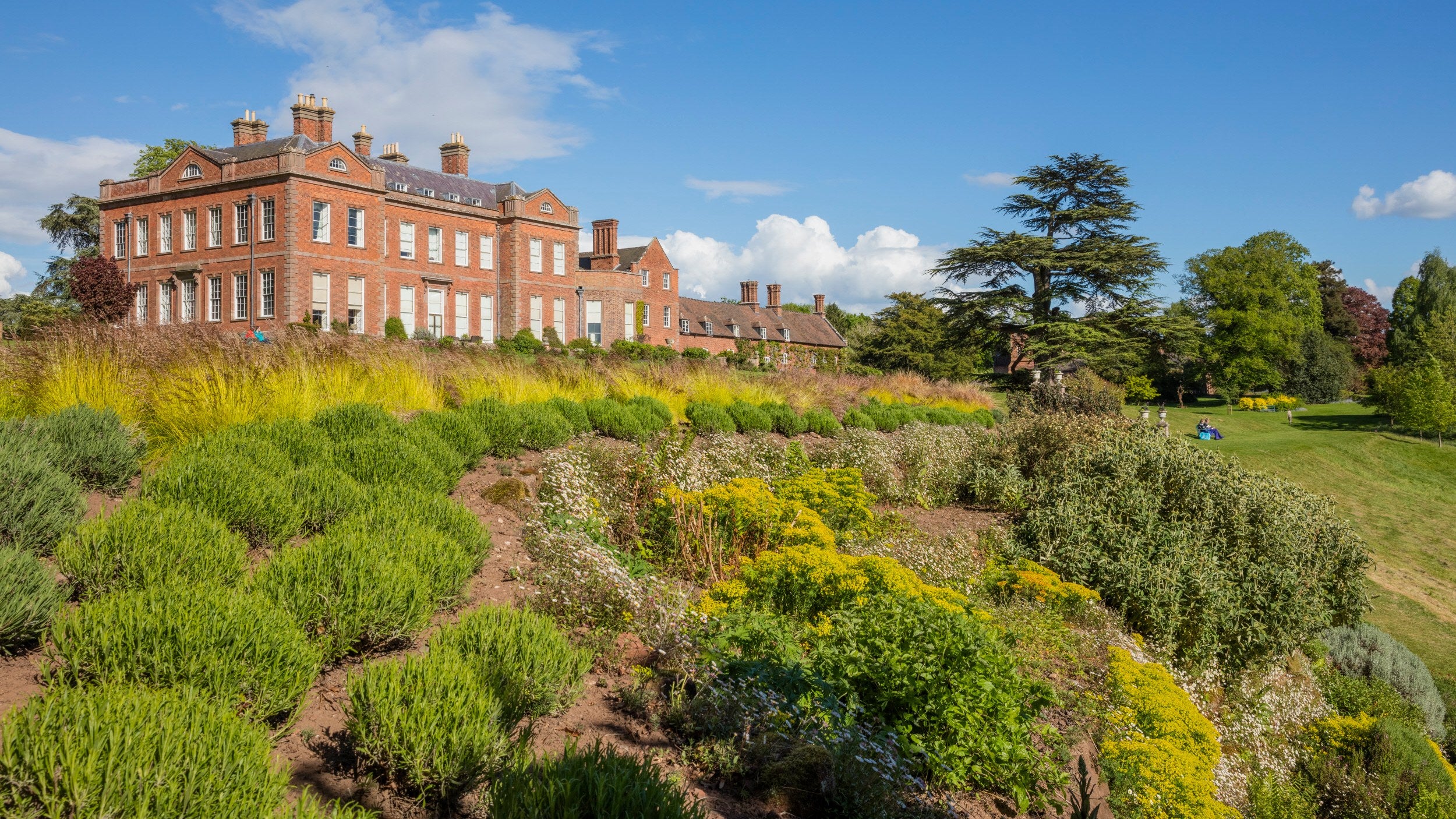 Blue skies and lush green gardens surround the red brick house of Dudmaston in Shropshire