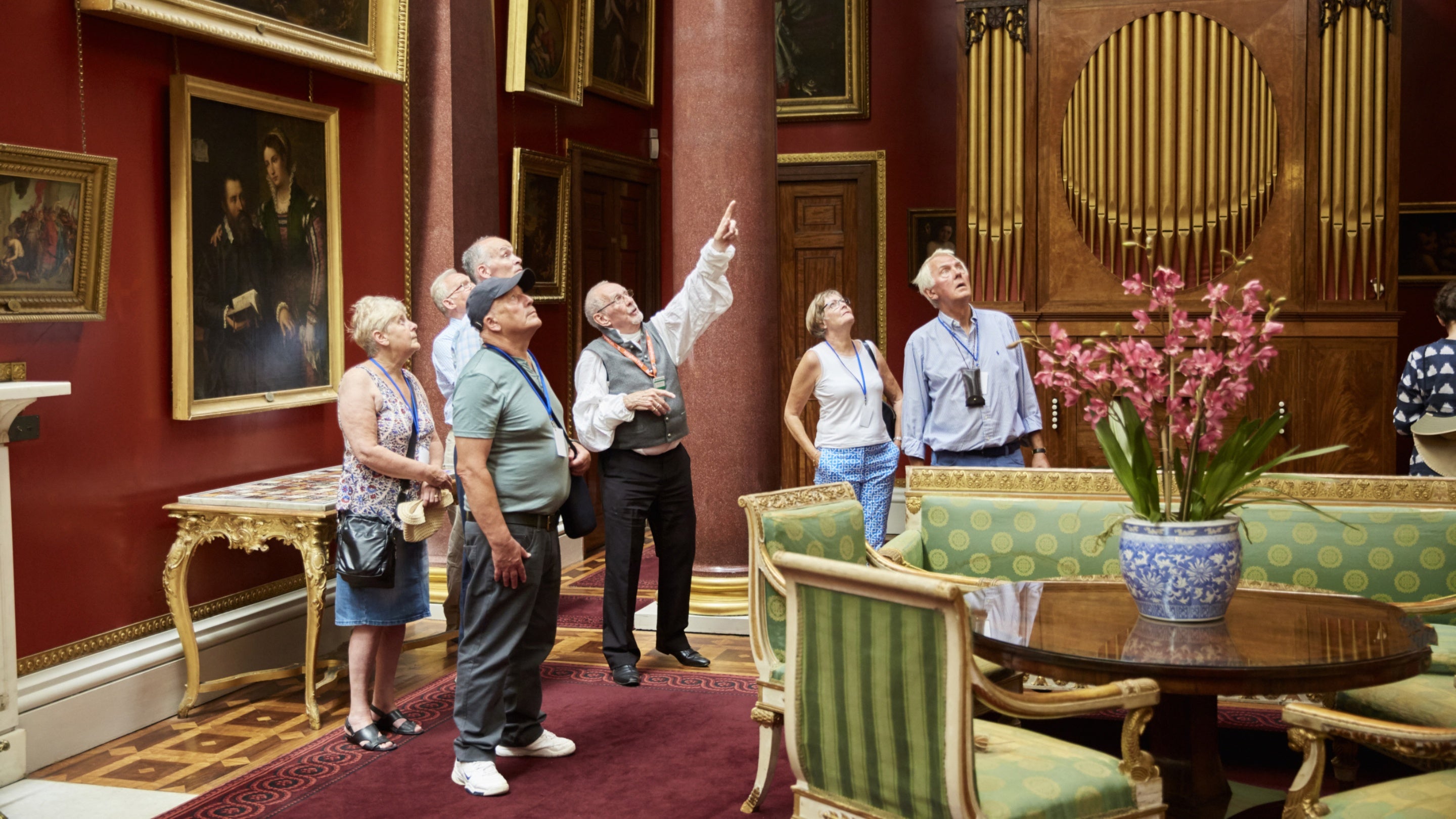 A group of visitors on a guided tour in the picture gallery at Attingham Park, Shropshire, looking up at the ceiling
