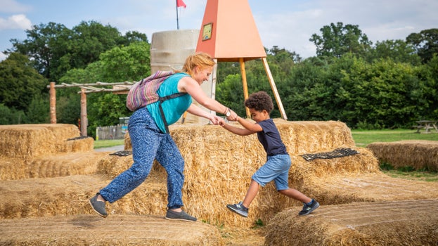 A parent and child play on a fort made of hay bales