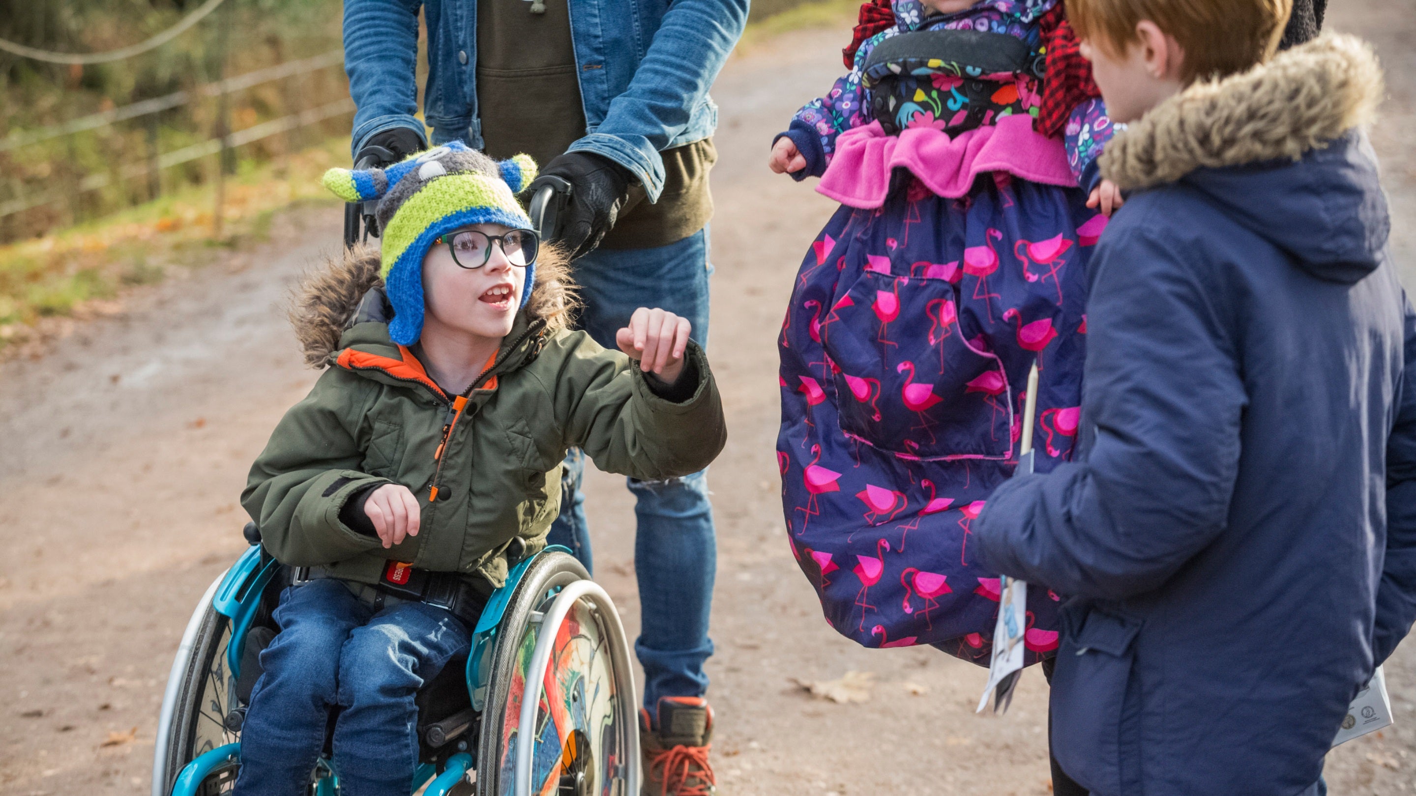 A child in a winter coat and hat, who is using a wheelchair, looks at a winter activity trail in the parkland at Attingham