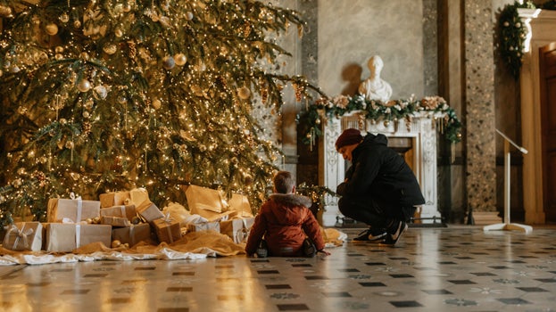 Man and boy crouched looking at a Christmas tree in the Entrance Hall at Attingham Park, Shropshire