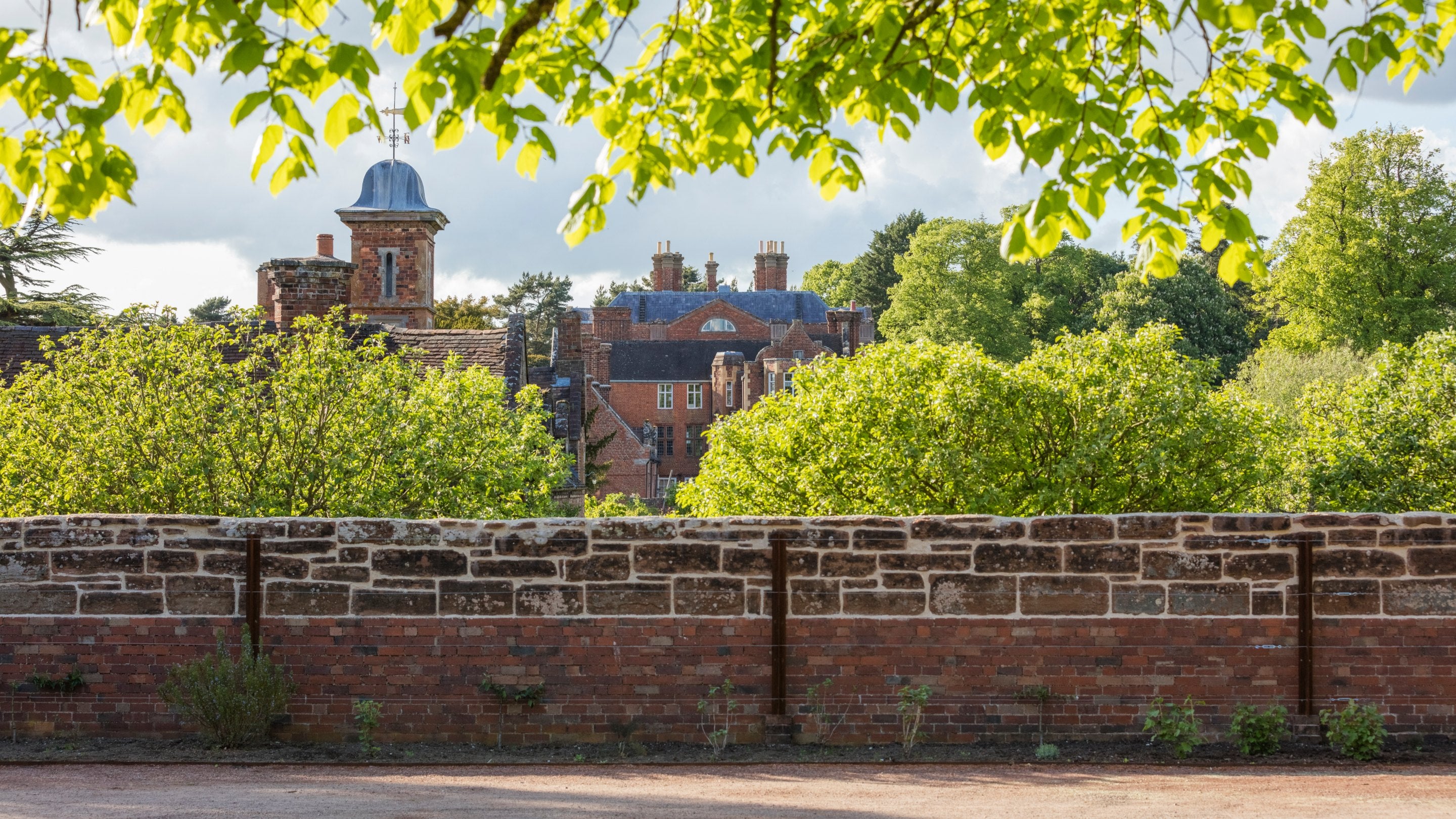 A view of the Stableyard and House at Dudmaston, Shropshire, from behind a red brick and stone wall.