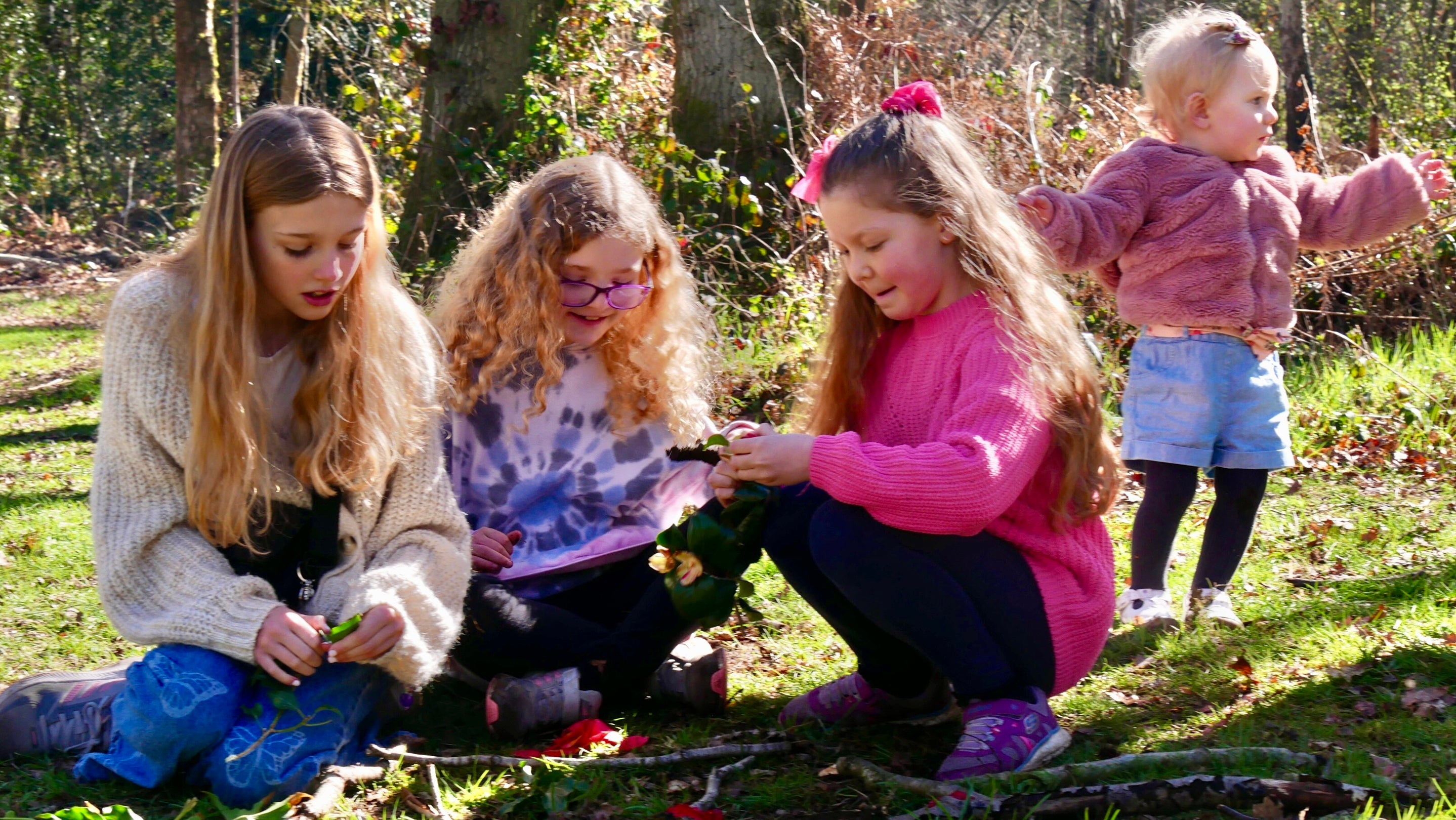 3 children make art out of sticks whilst a younger child behind them looks into distance
