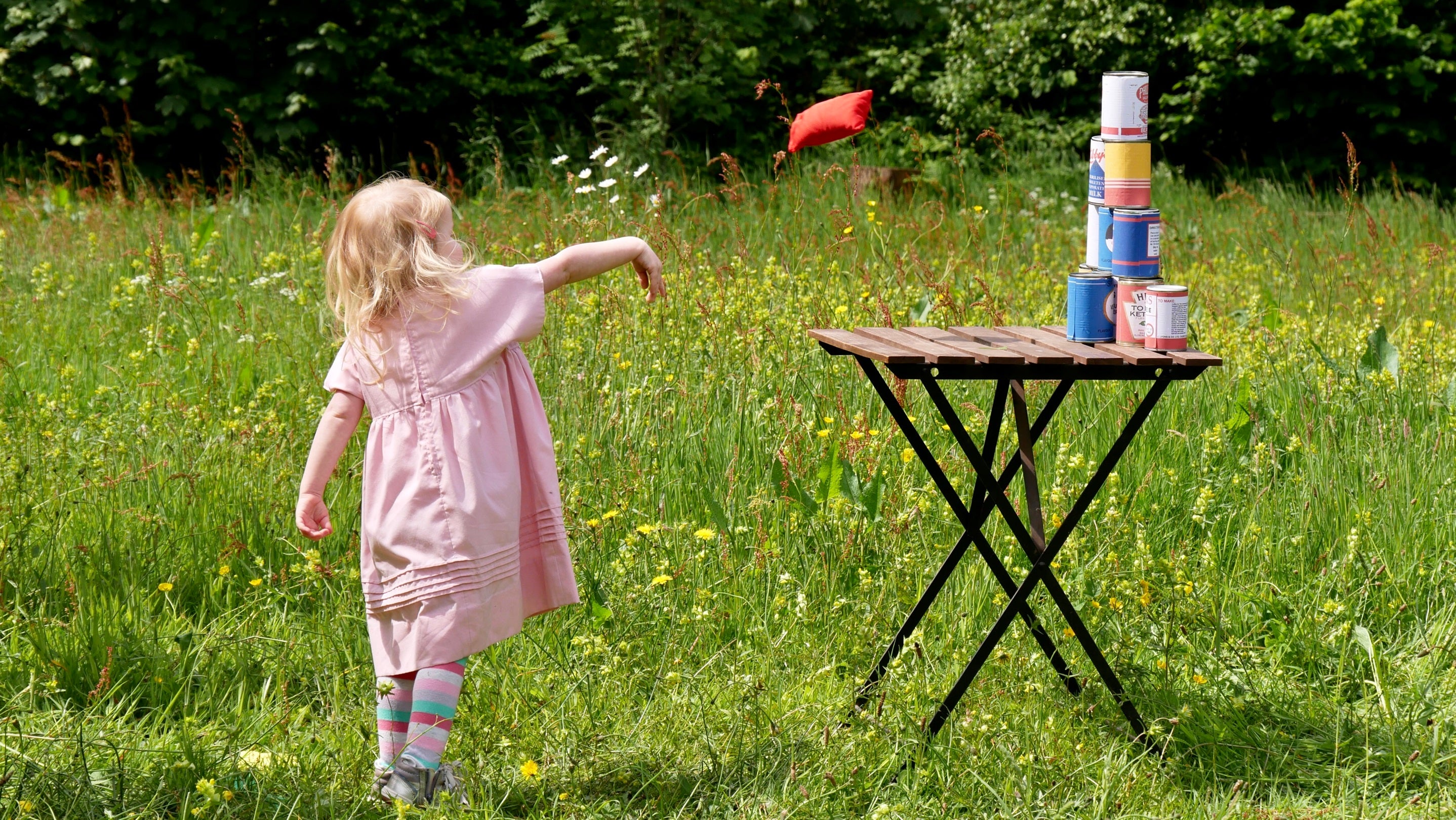 Young child throwing a beanbag in a wildflower meadow.