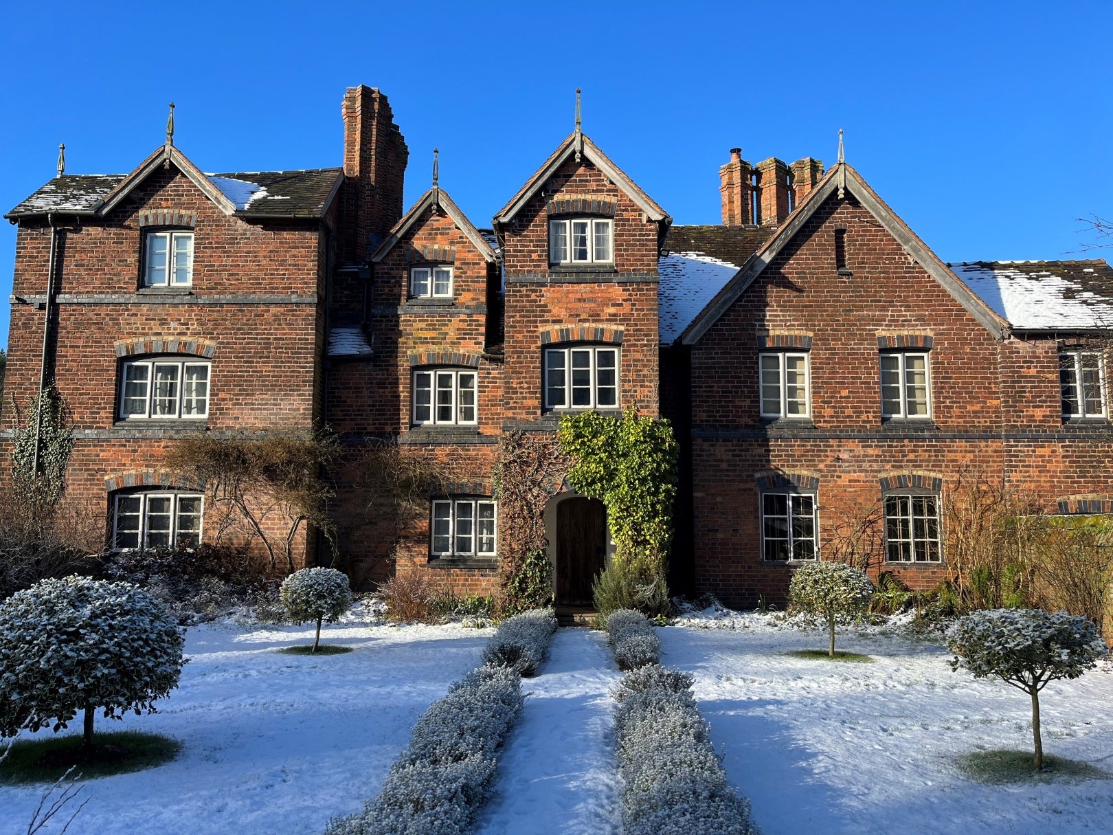 The front of Moseley Old Hall in the winter sun. The sky is a deep blue and the grass infront of the house is covered with morning frost