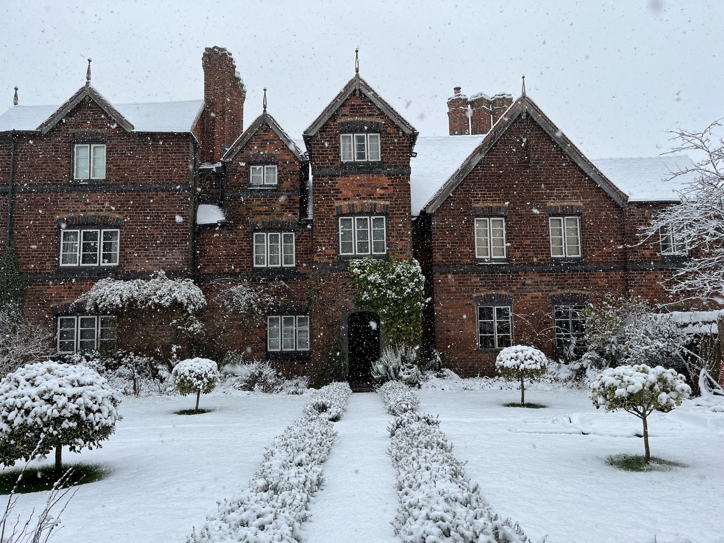 The front exterior of Moseley Old Hall with snow on the ground and roof of the building. Snow is also seen falling in the image.