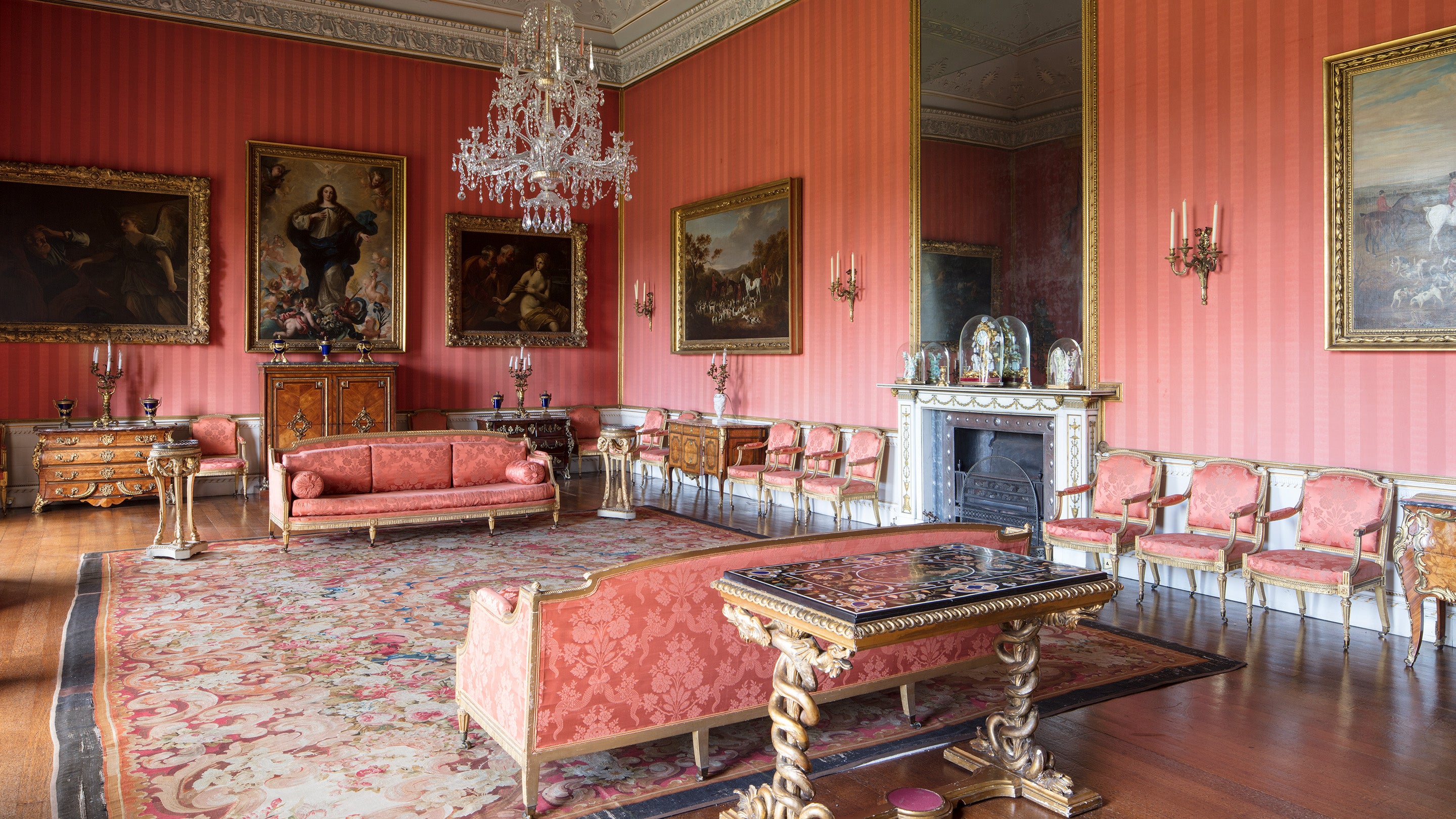 The Red Drawing Room, decorated with red wallpaper, a large rug with red to pink patterns, all of the furniture is also upholstered in a pinky-red brocade fabric.