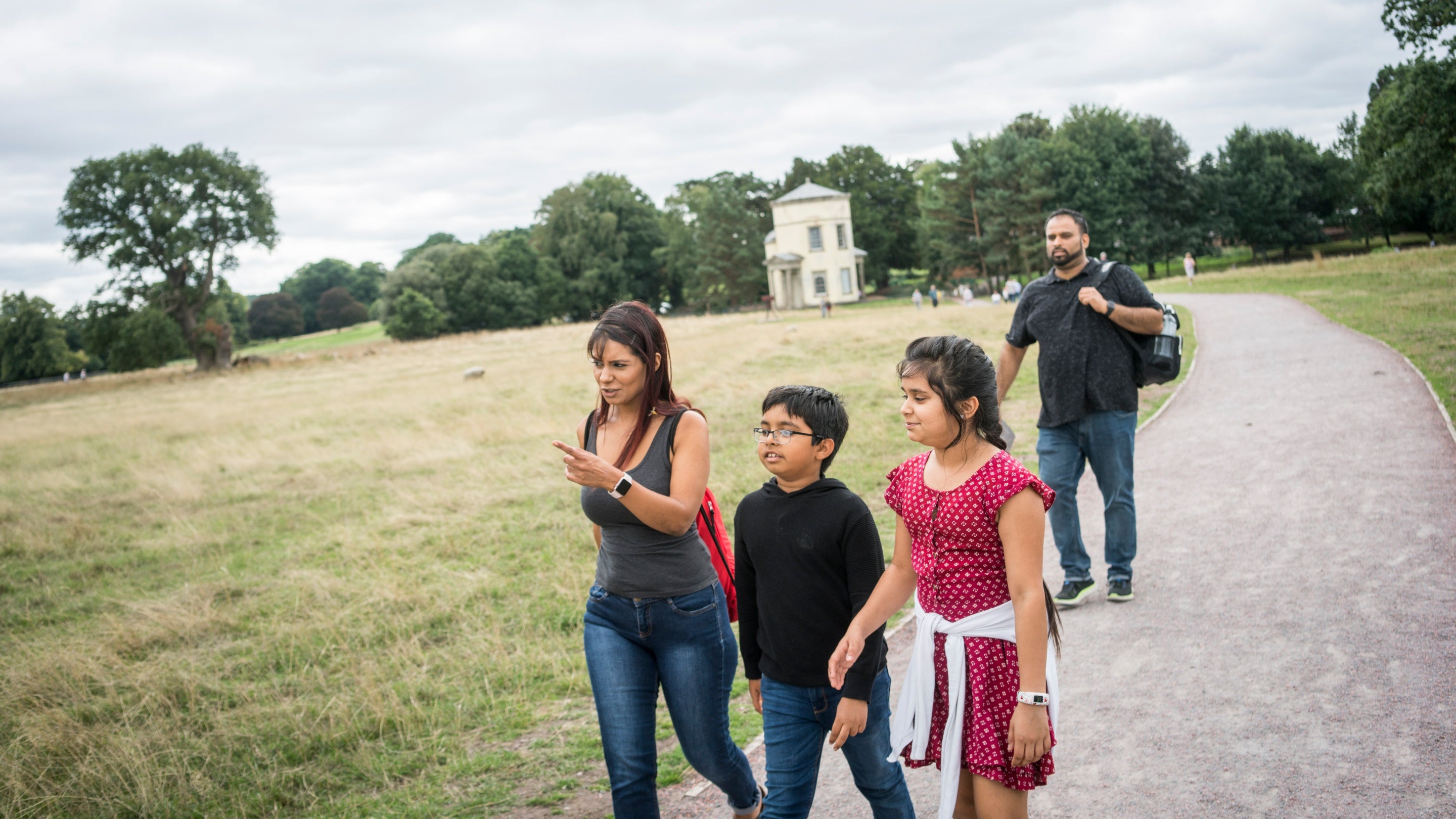 Two adults and two children walk along a path through the parkland at Shugborough Estate, Staffordshire