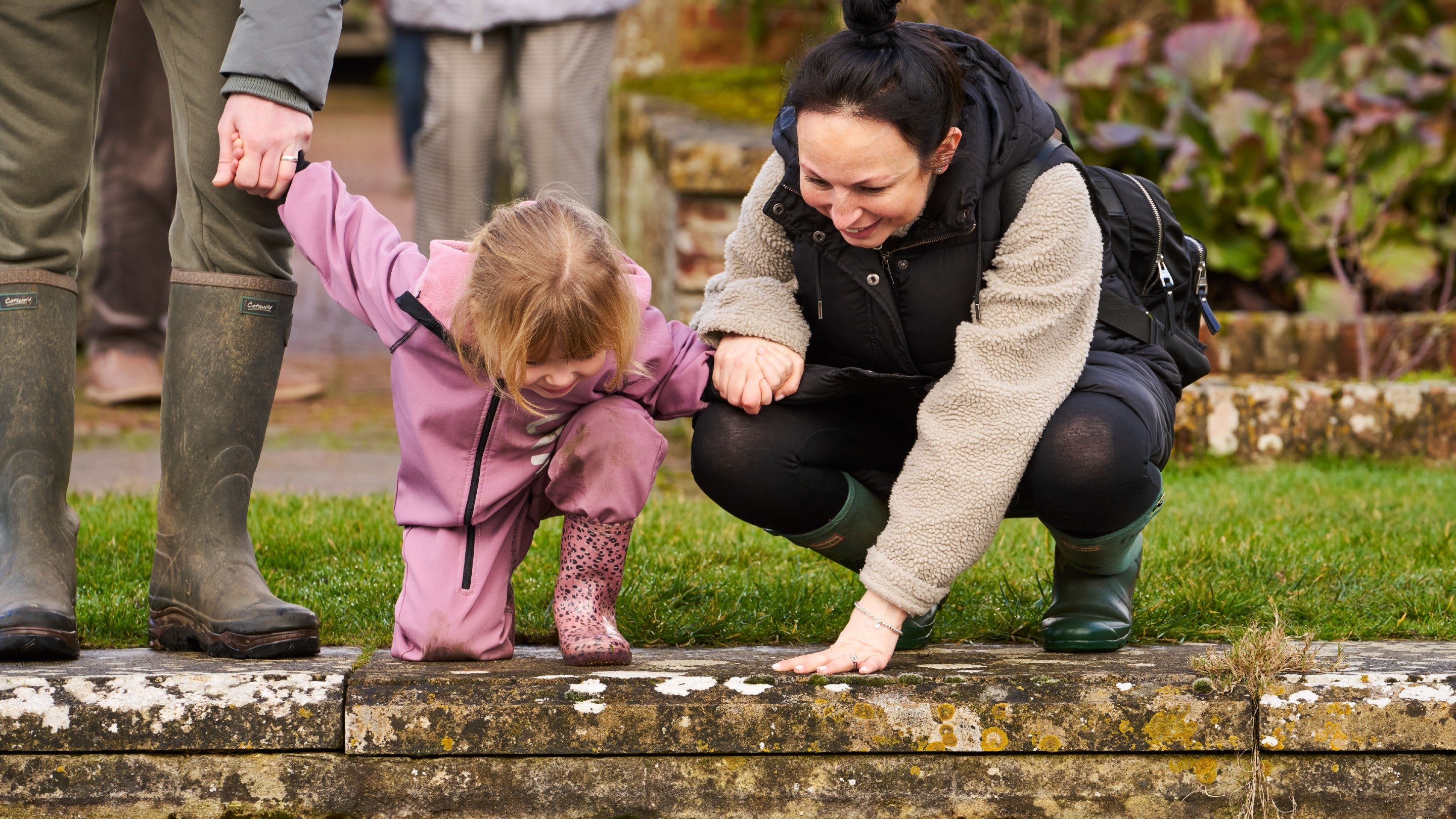 Adult and child bent down looking into a pond