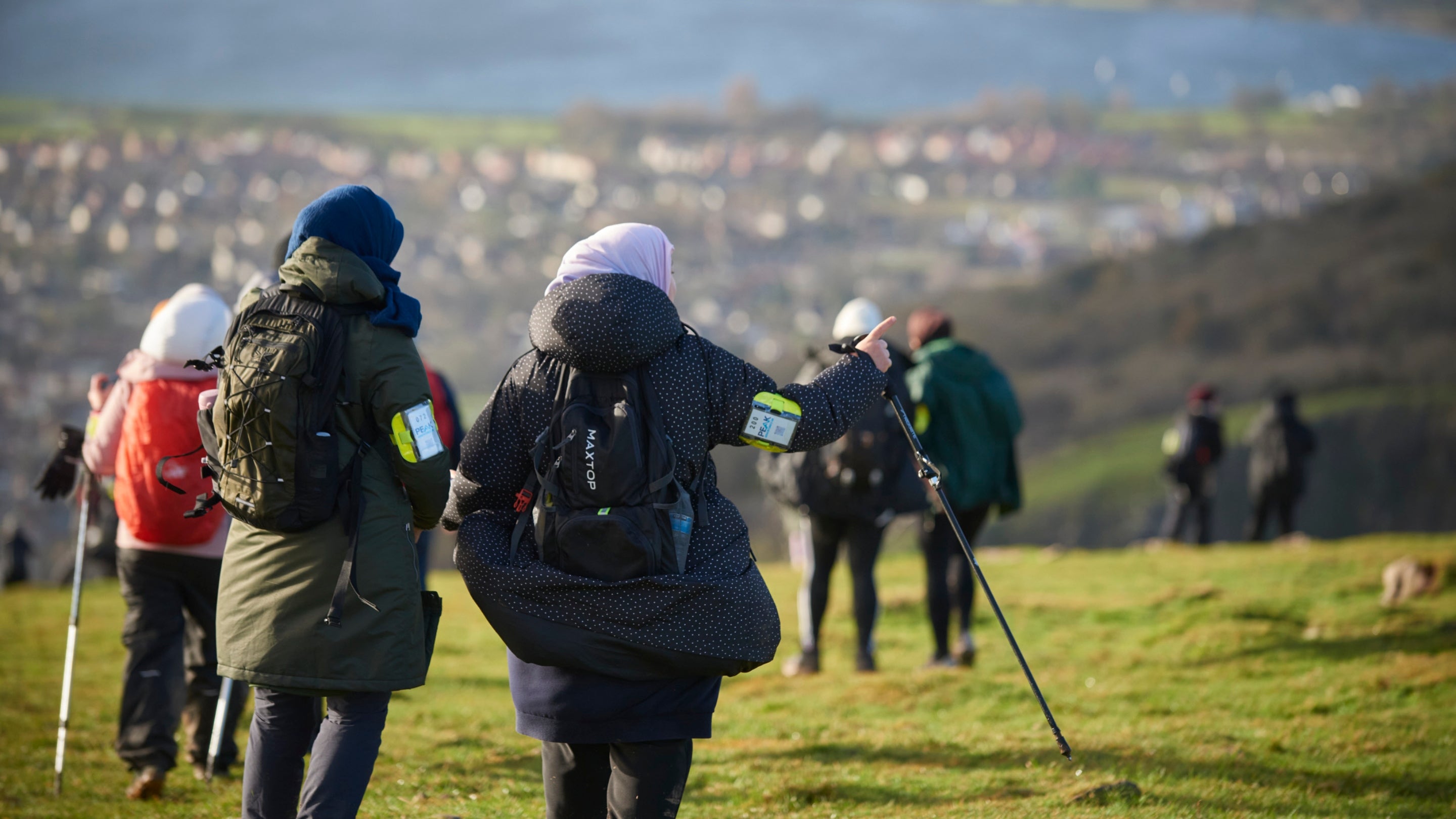 Walkers at the top of a cliff looking down at the view of a town and resevoir