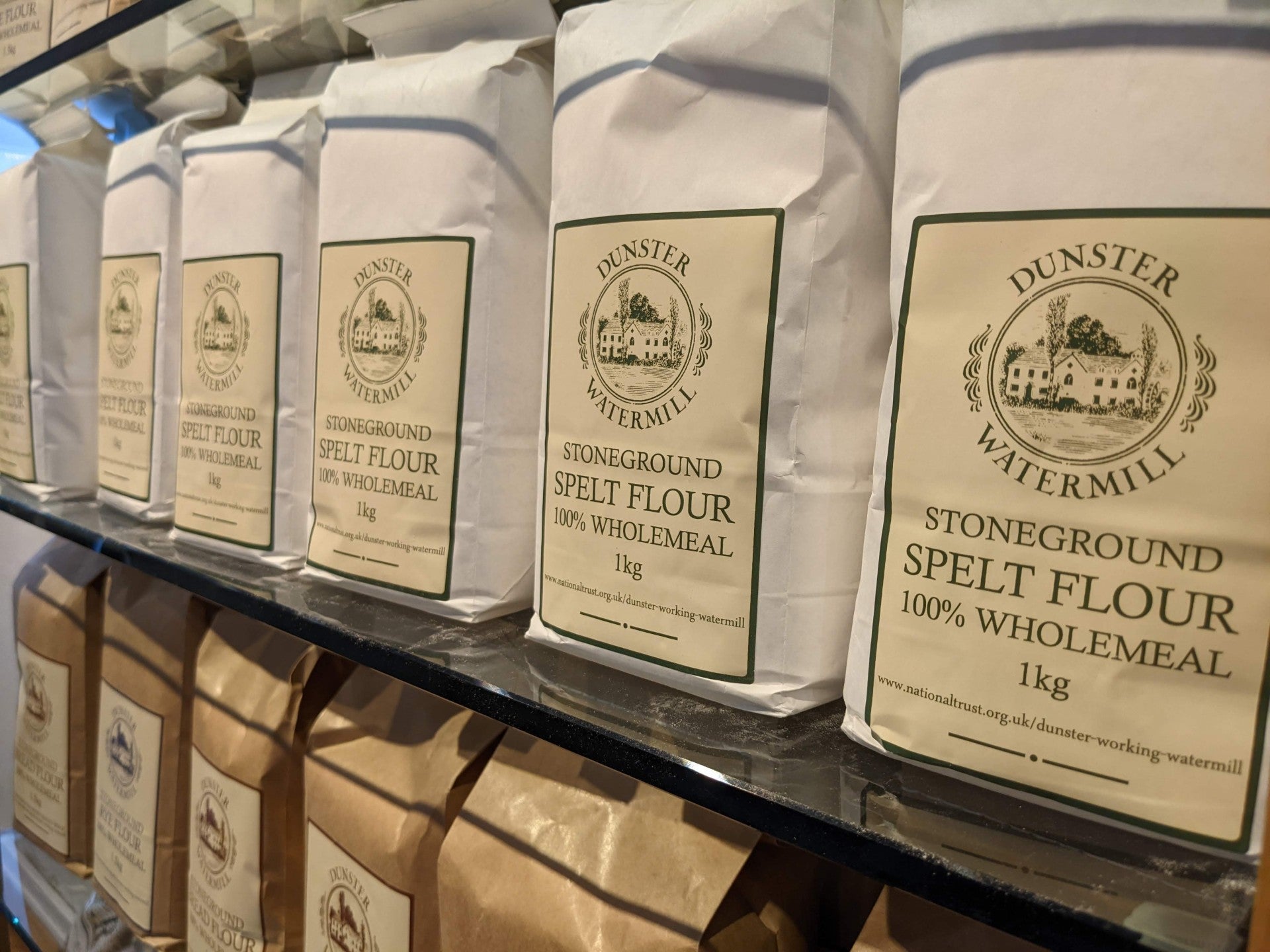 A photograph of white bags of spelt flour milled at Dunster Working Watermill displayed on a shelf in the Stables Shop