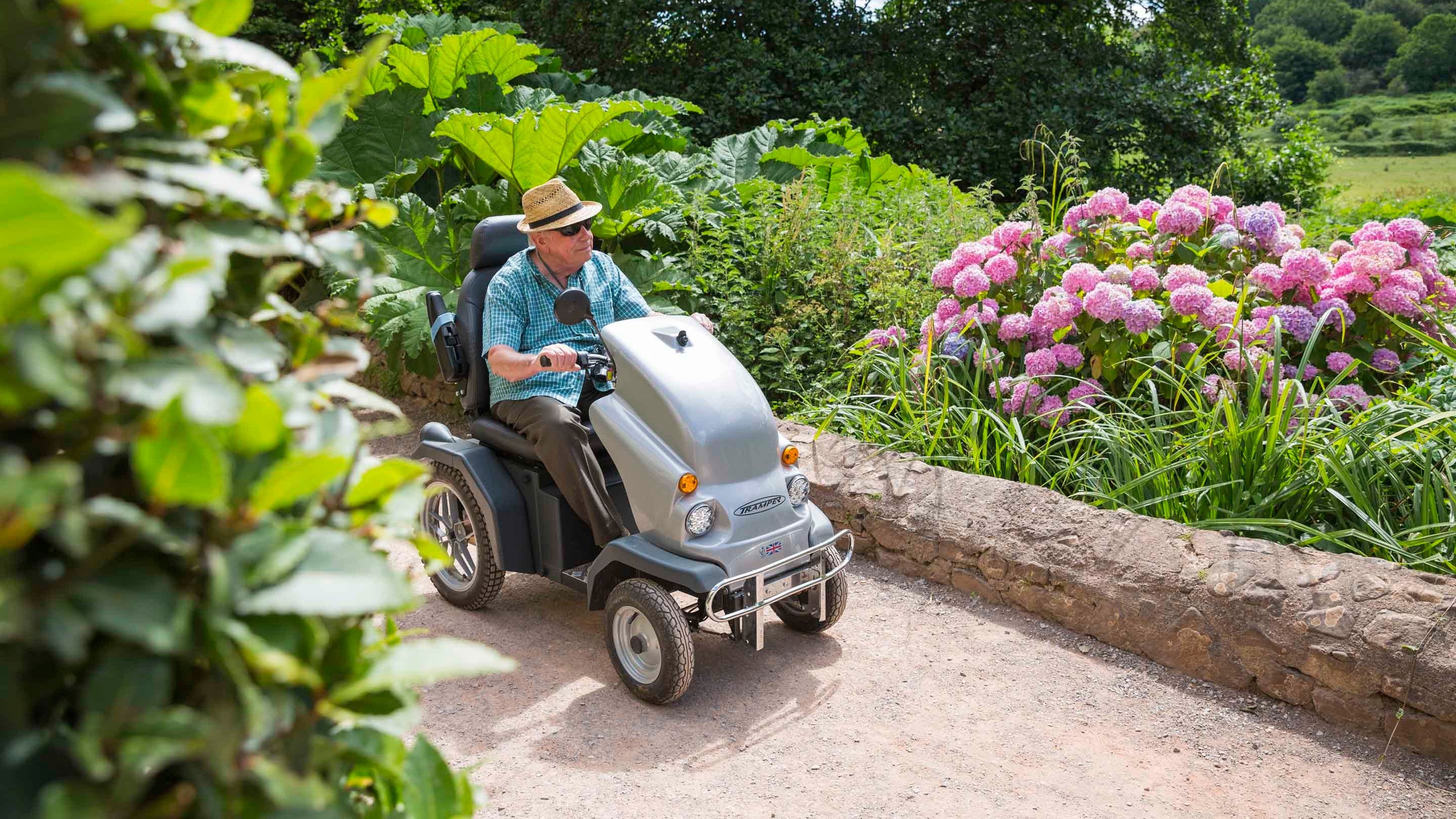 A visitor in a mobility scooter explores a pathway in the garden at Dunster Castle, Somerset