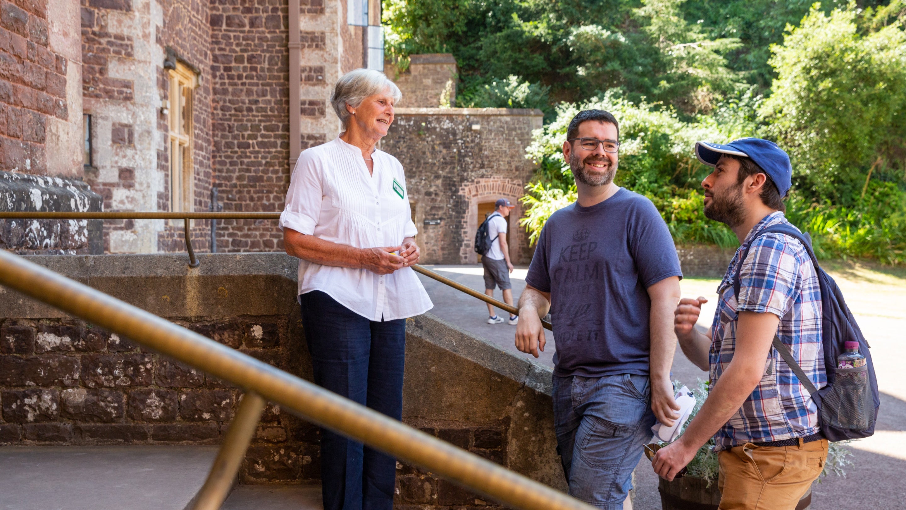 A volunteer welcomes two visitors at the entrance to Dunster Castle, Somerset