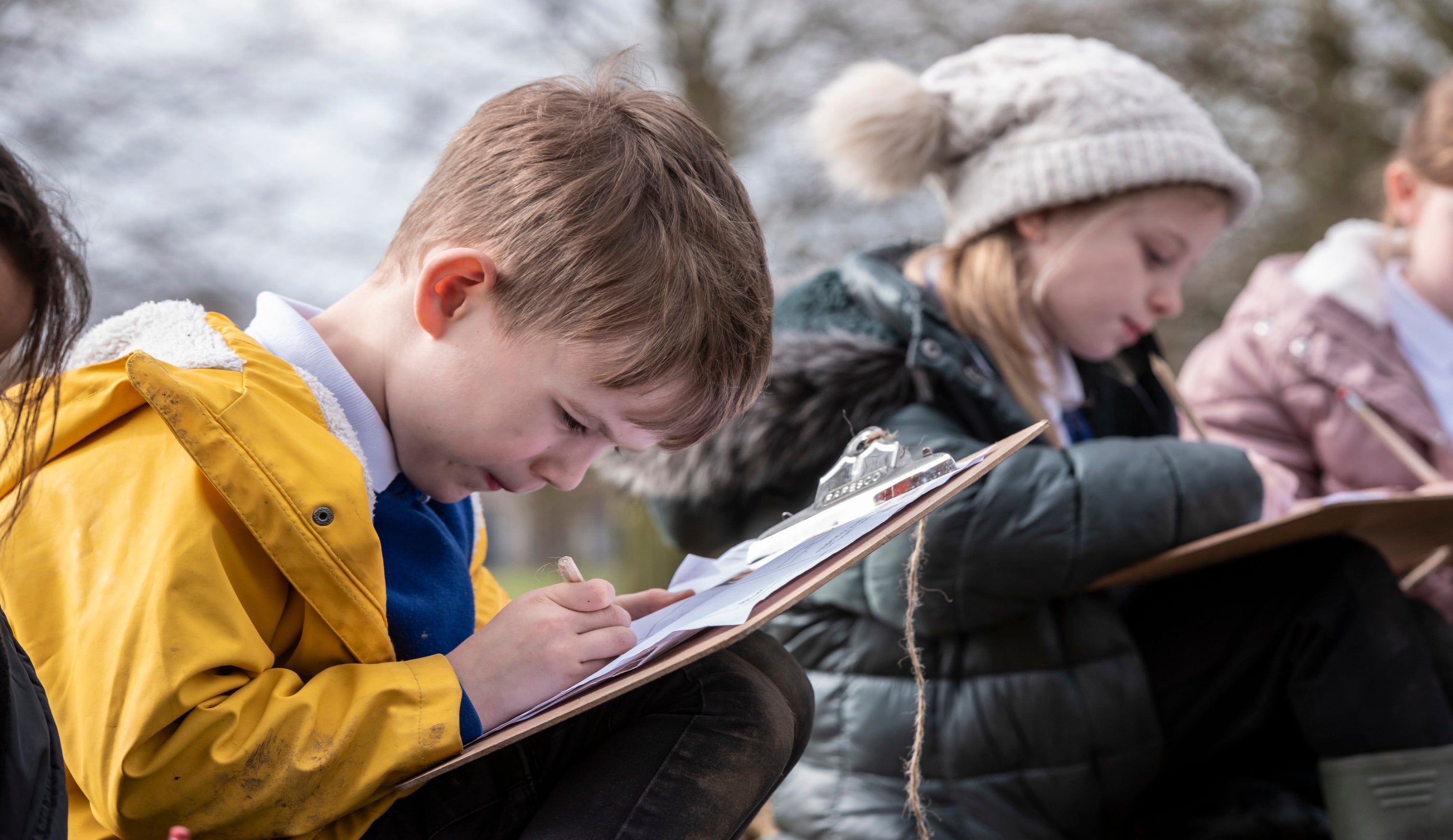 Two primary school children on their 'Eco Walk' in the park, filling in a worksheet on their clipboards.