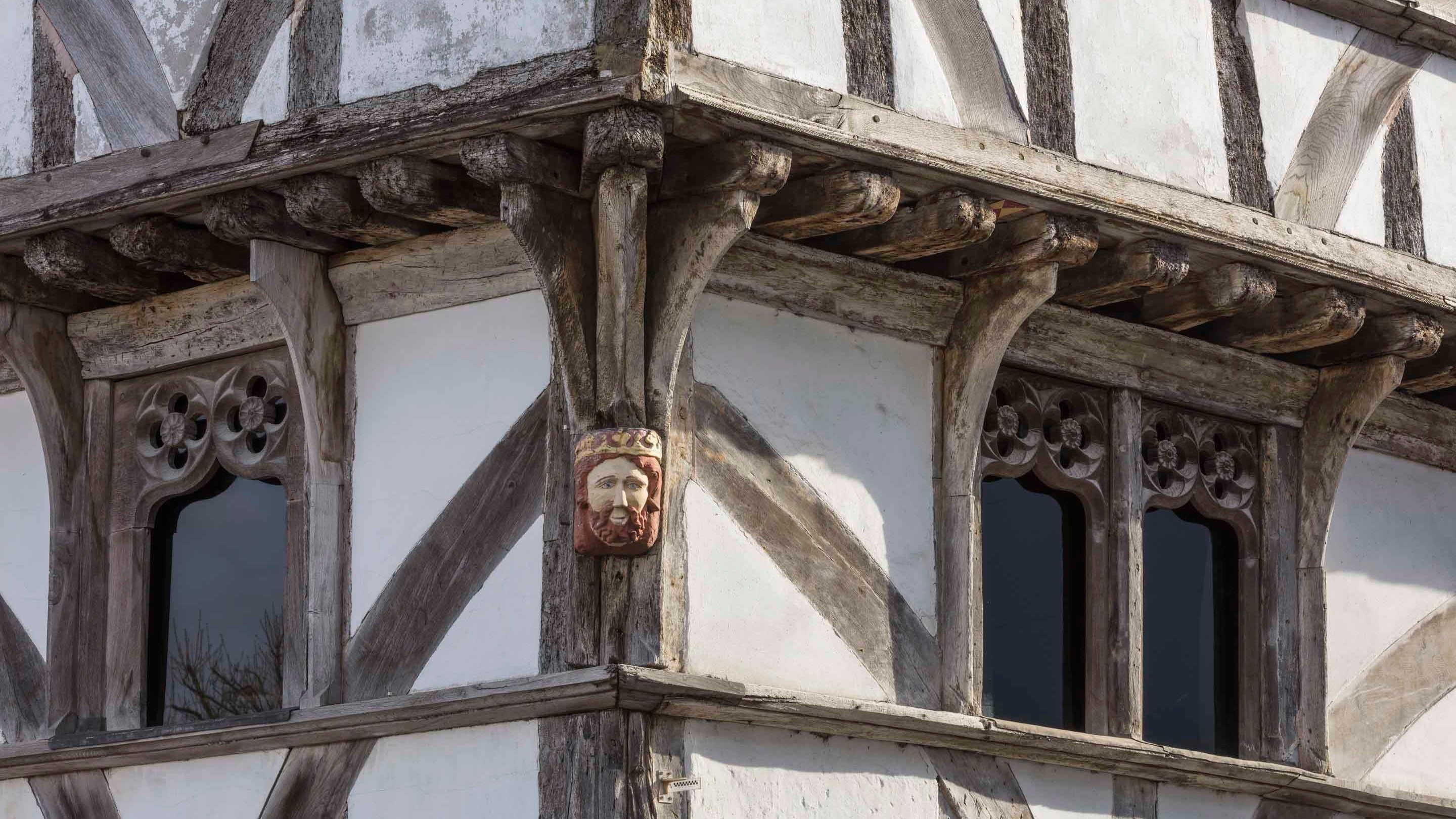 A close-up of timber on the exterior of King John's Hunting Lodge, Somerset, with the wooden face of a man wearing a crown attached to it.