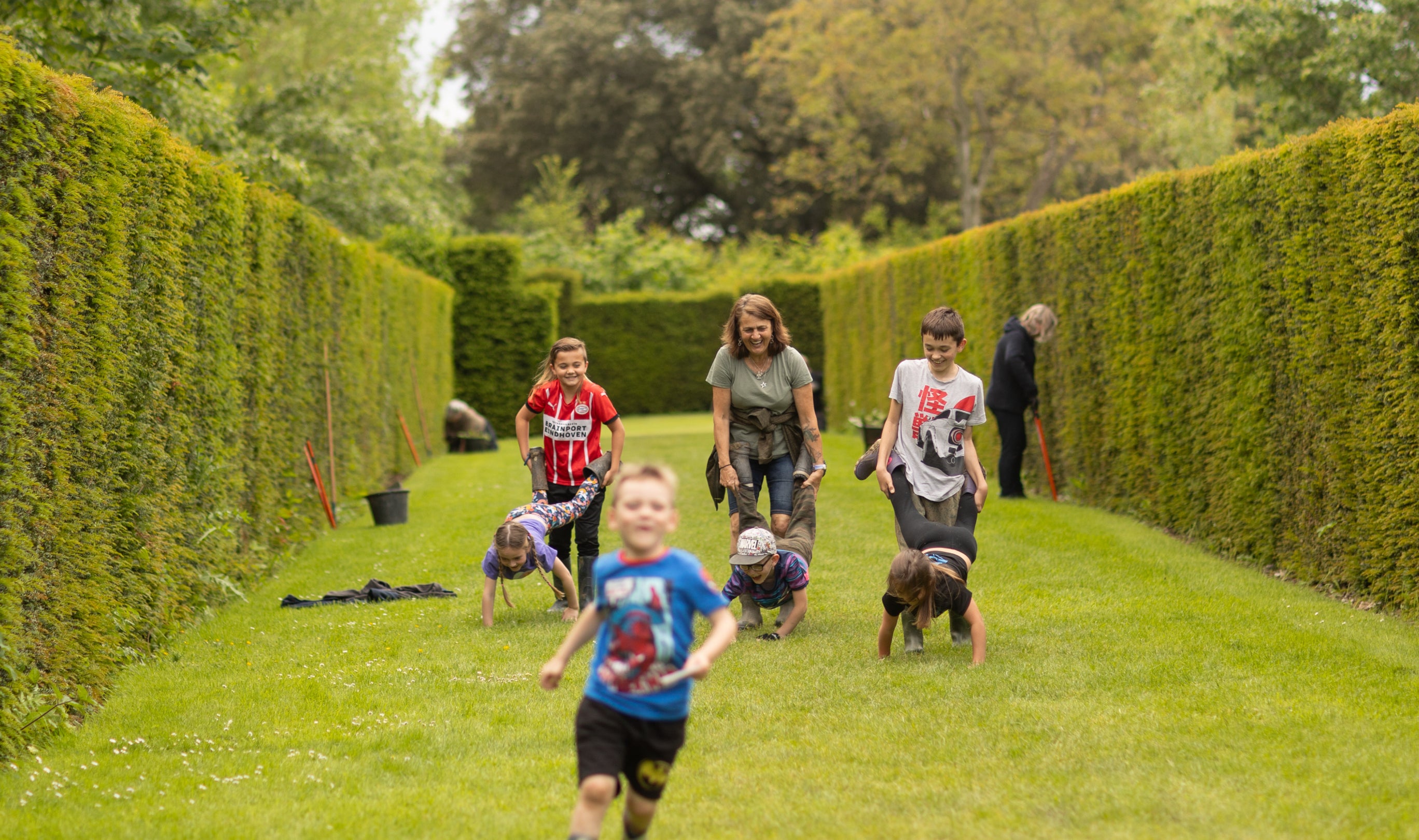 Family running and playing wheelbarrows in the garden, Lytes Cary Manor, Somerset