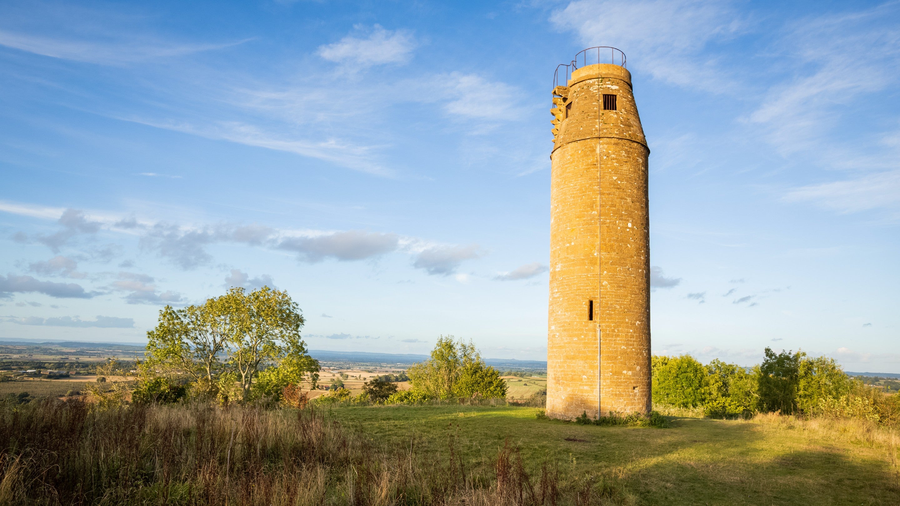A tall stone tower on level ground at the top of a hill - there are views across open countryside behind