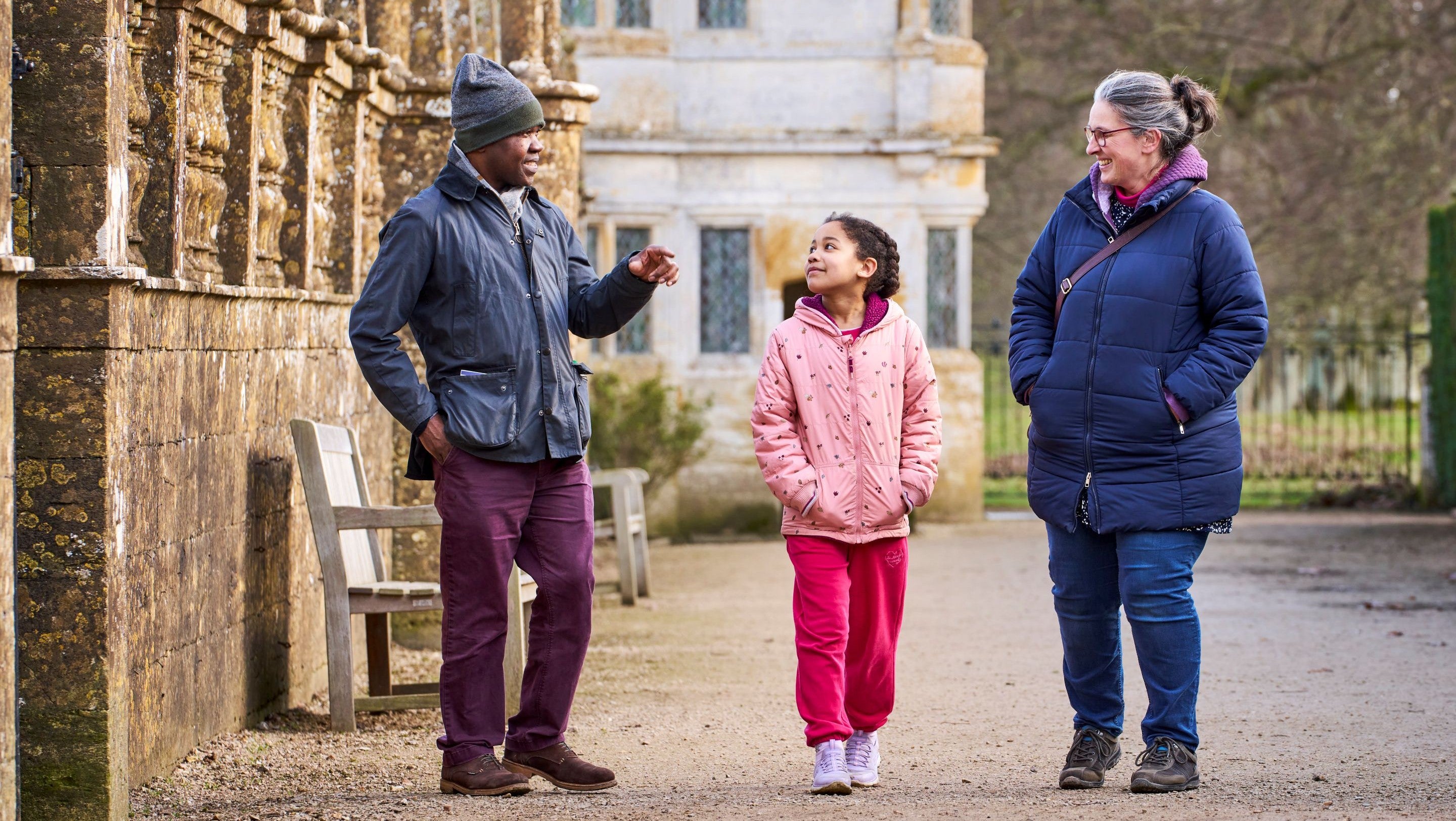 A family of three talking and walking past a balustraded wall at Montacute House