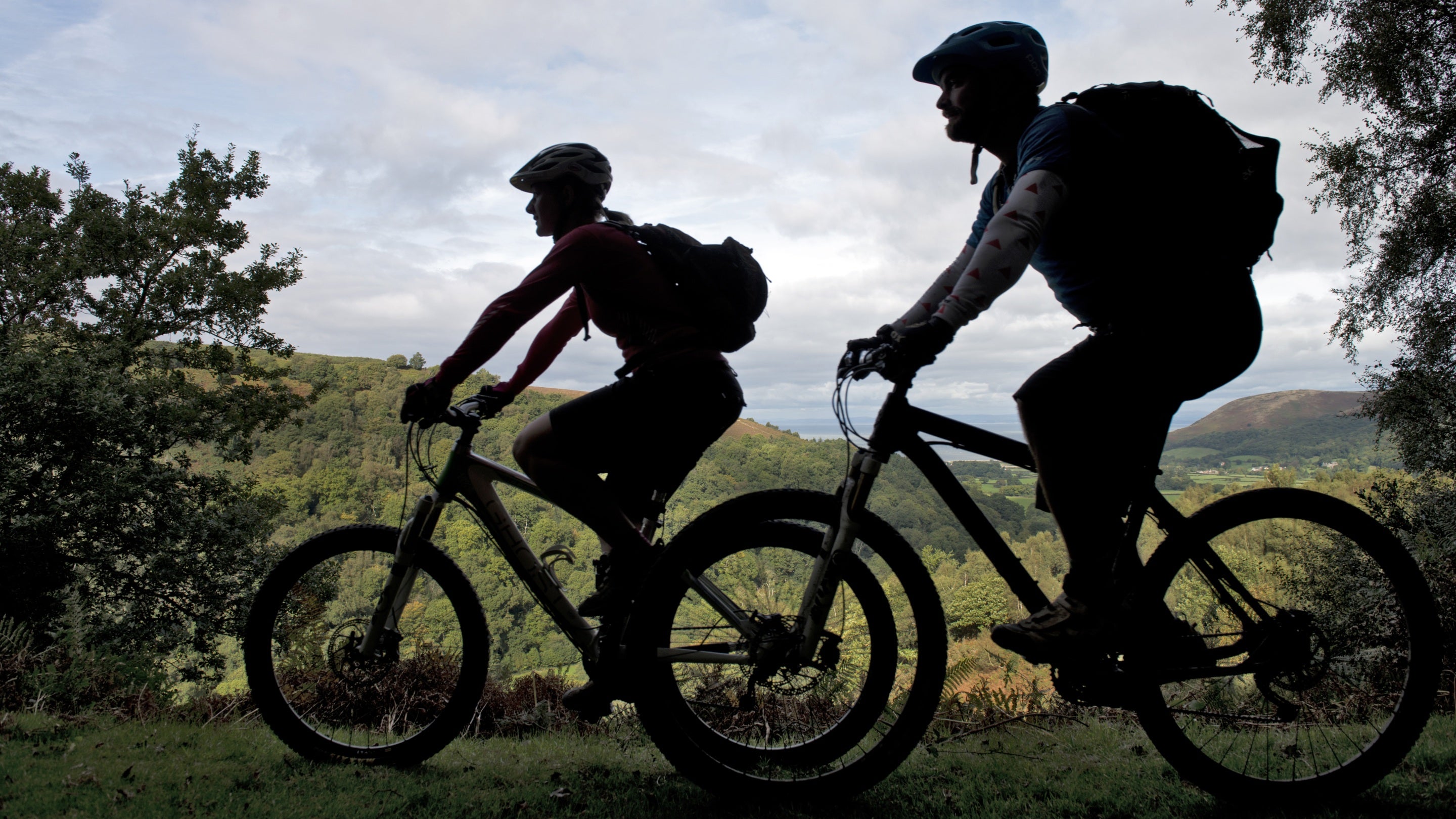 Silhouettes of two mountain bikers riding near Webber's Post on the Holnicote Estate, Exmoor National Park, Somerset