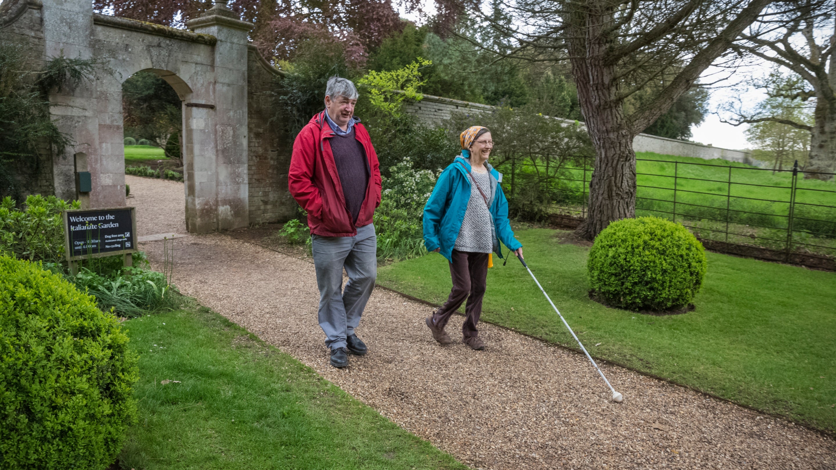 A visually impaired lady walks with a man in the formal gardens at Ickworth, Suffolk