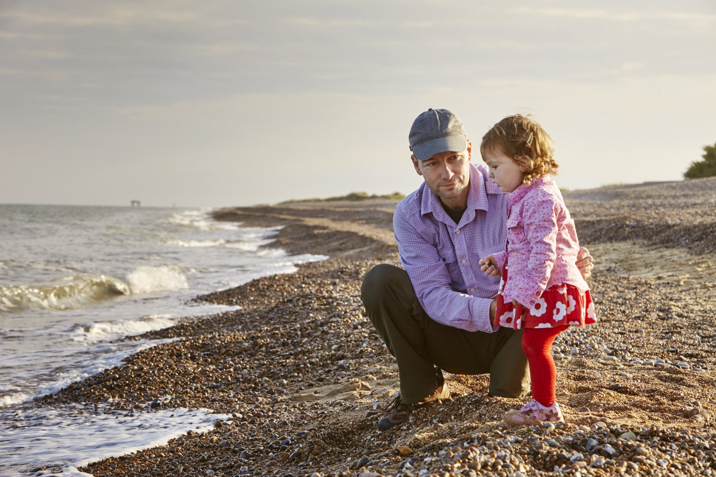 A father crouched down beside his daughter on the shoreline at Dunwich Beach