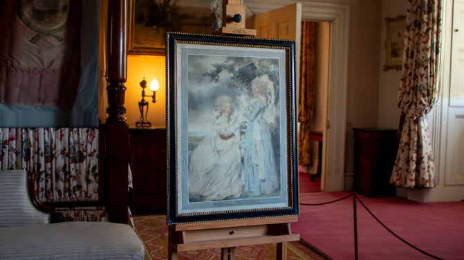 A watercolour of two women in georgian dress in a black frame. It is on a wooden easel in a bedroom
