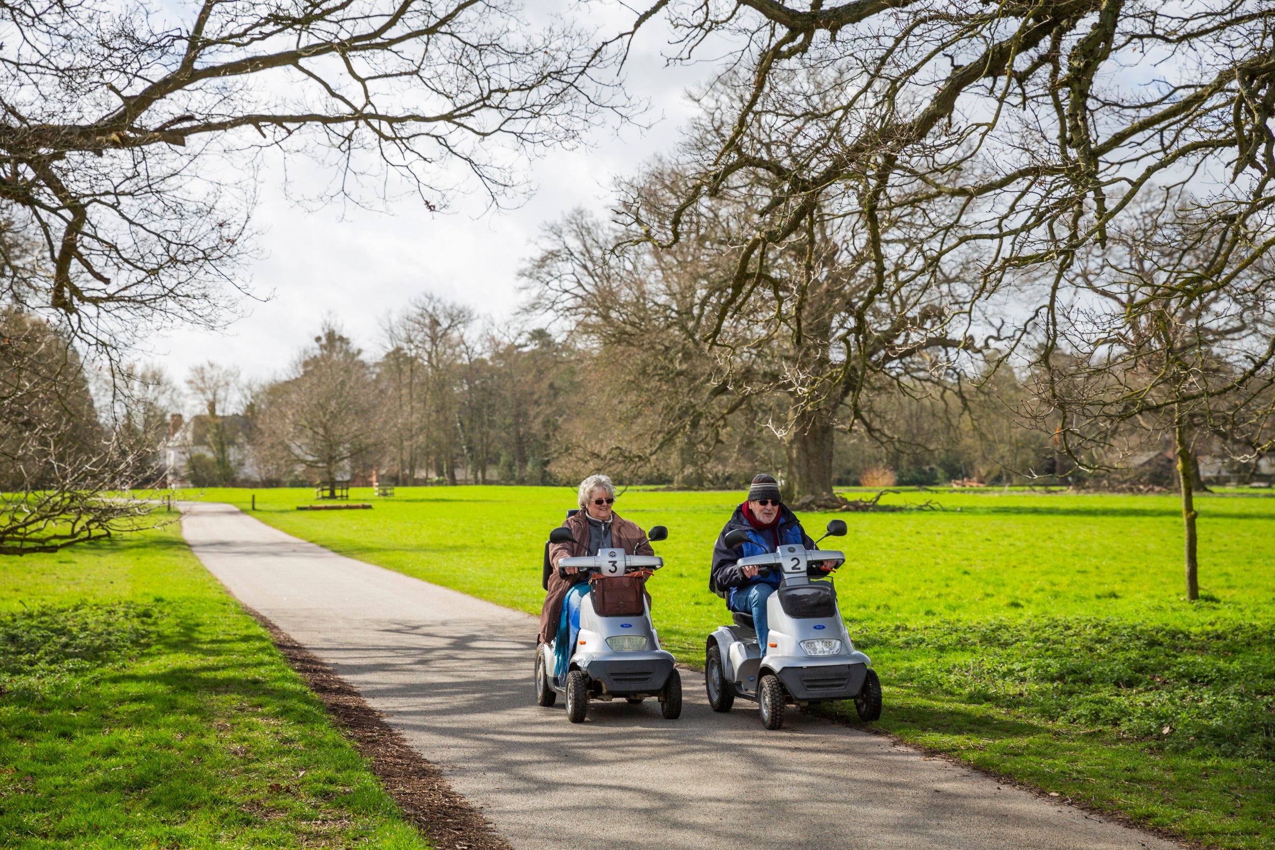 Two people in mobile trampers exploring along a level path through winter parkland