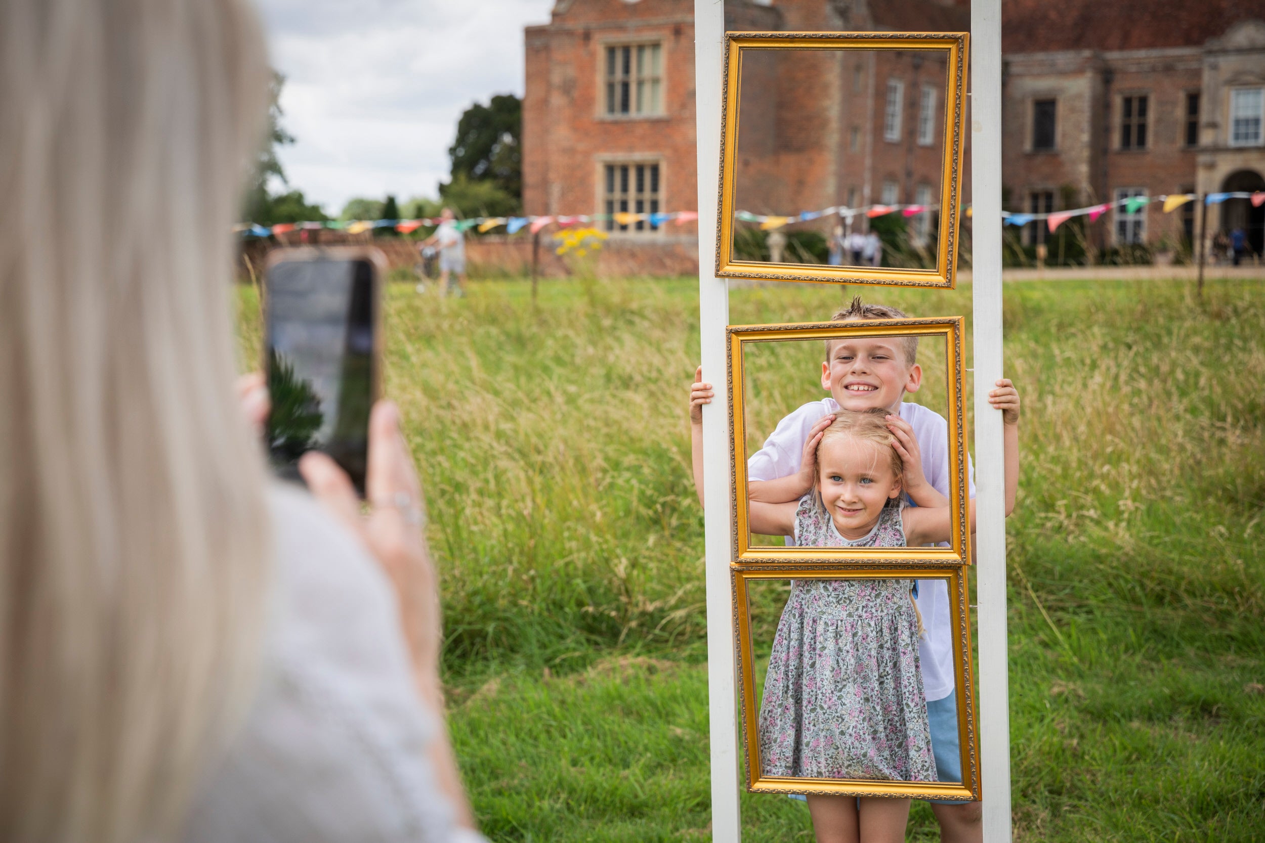 A parent photographs two children as they pose for a photograph while filling an empty picture frame