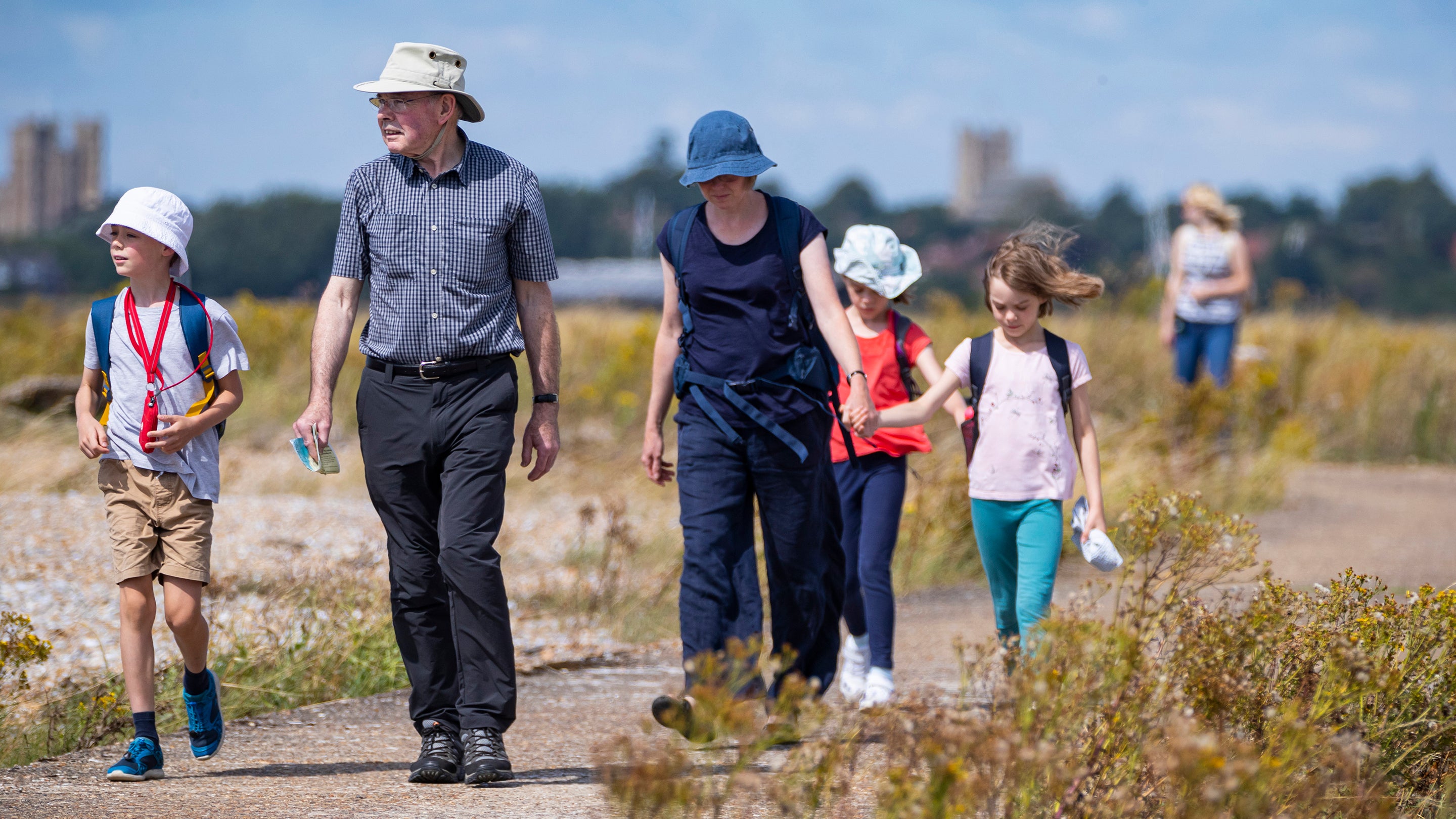 a multi-generational family walking on a concrete path on a sunny day at Orford Ness National Nature Reserve, Suffolk