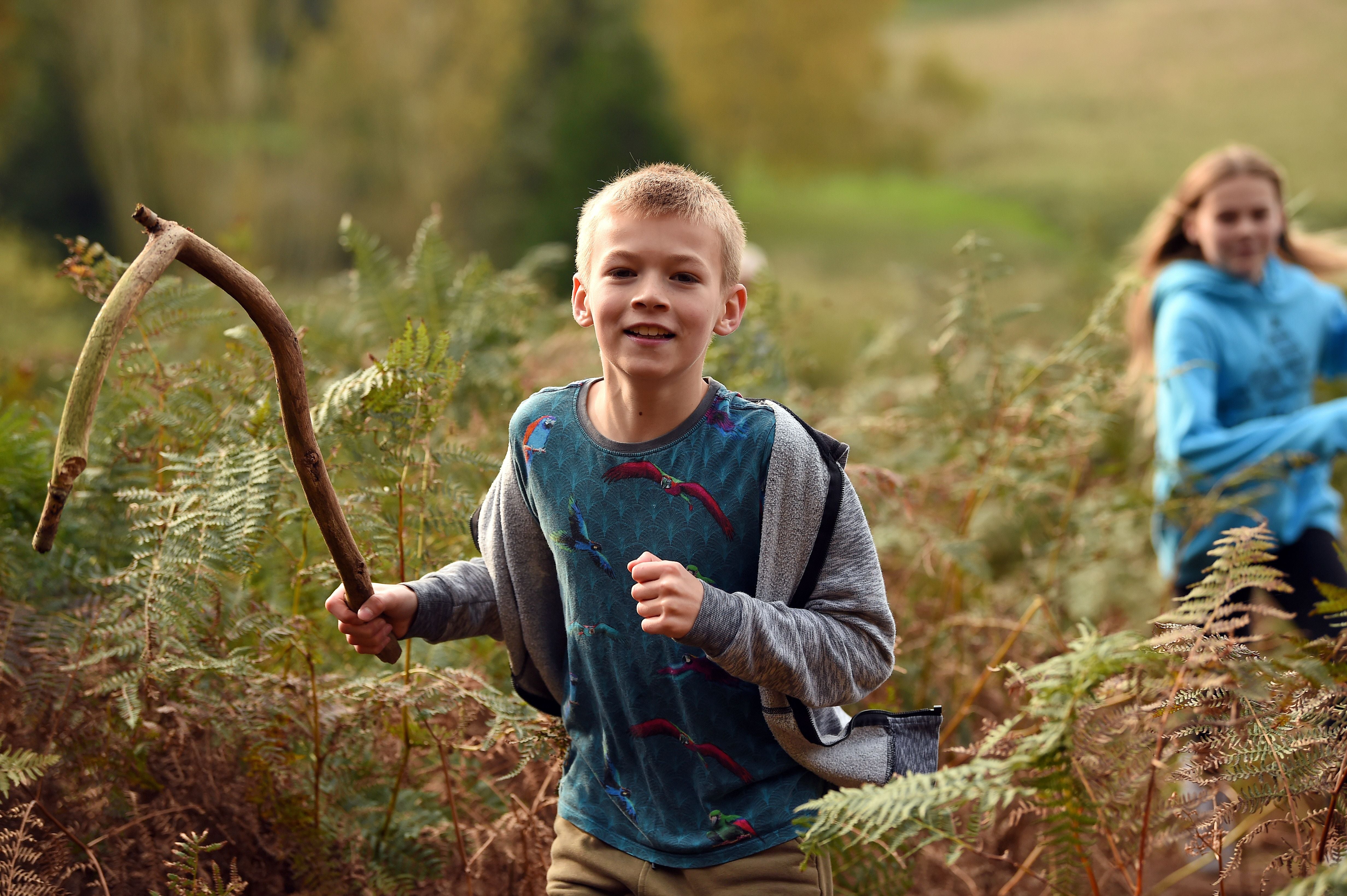 A boy running through woodland at Sutton Hoo holding a long stick