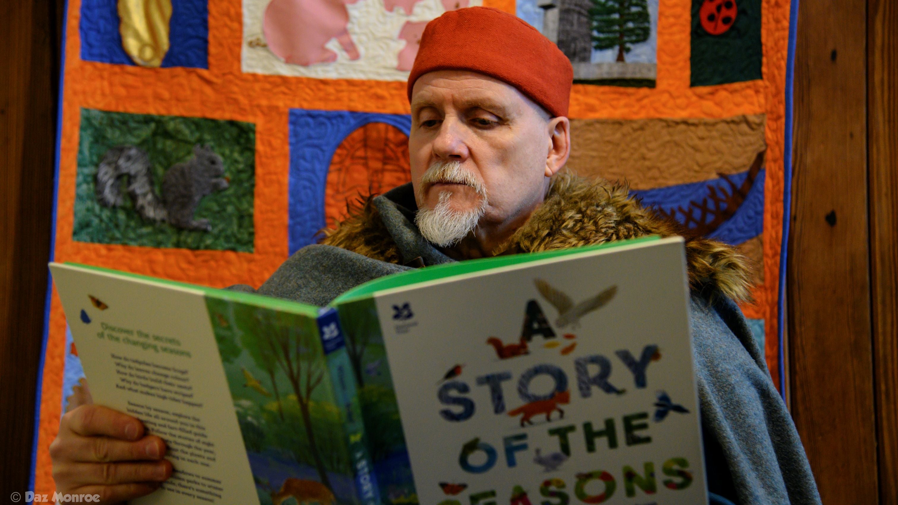 A man dressed up as an Anglo-Saxon warrior while reading a National Trust book, A Story of the Seasons, inside a converted stable
