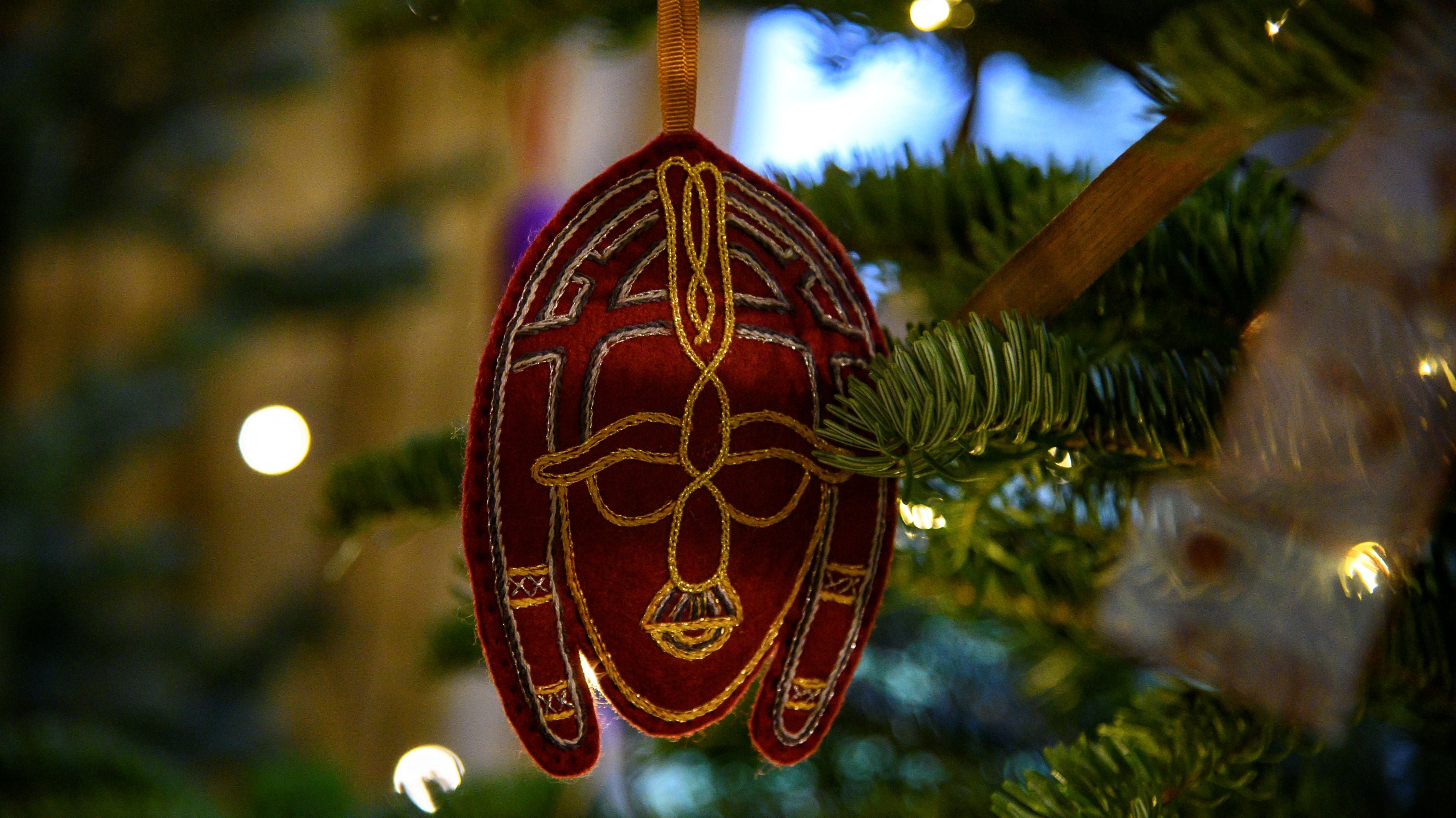 Close-up of a burgundy coloured felt decoration, embroidered with gold thread, hanging from a fir tree branch inside Tranmer House