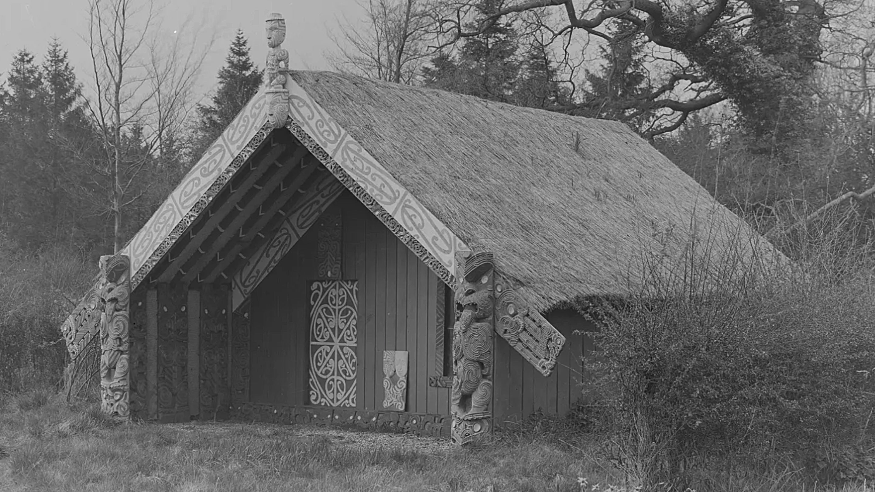 A black and white image of a gabled Maori meeting house with a thatched roof