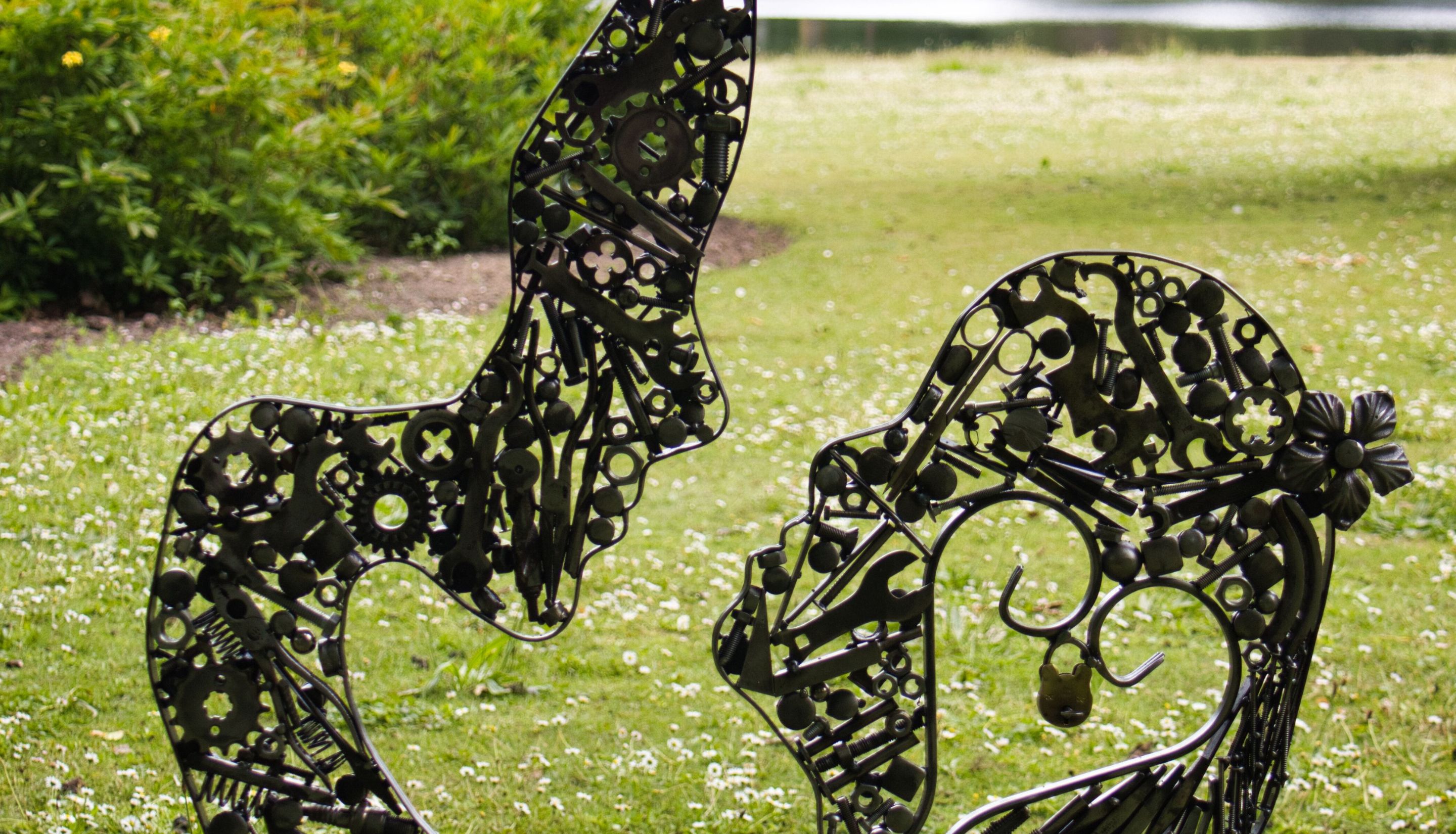 The image shows two metal sculptures of human profiles facing each other. The sculptures are intricately designed with various shapes and patterns, including circles, crosses, and other geometric forms.