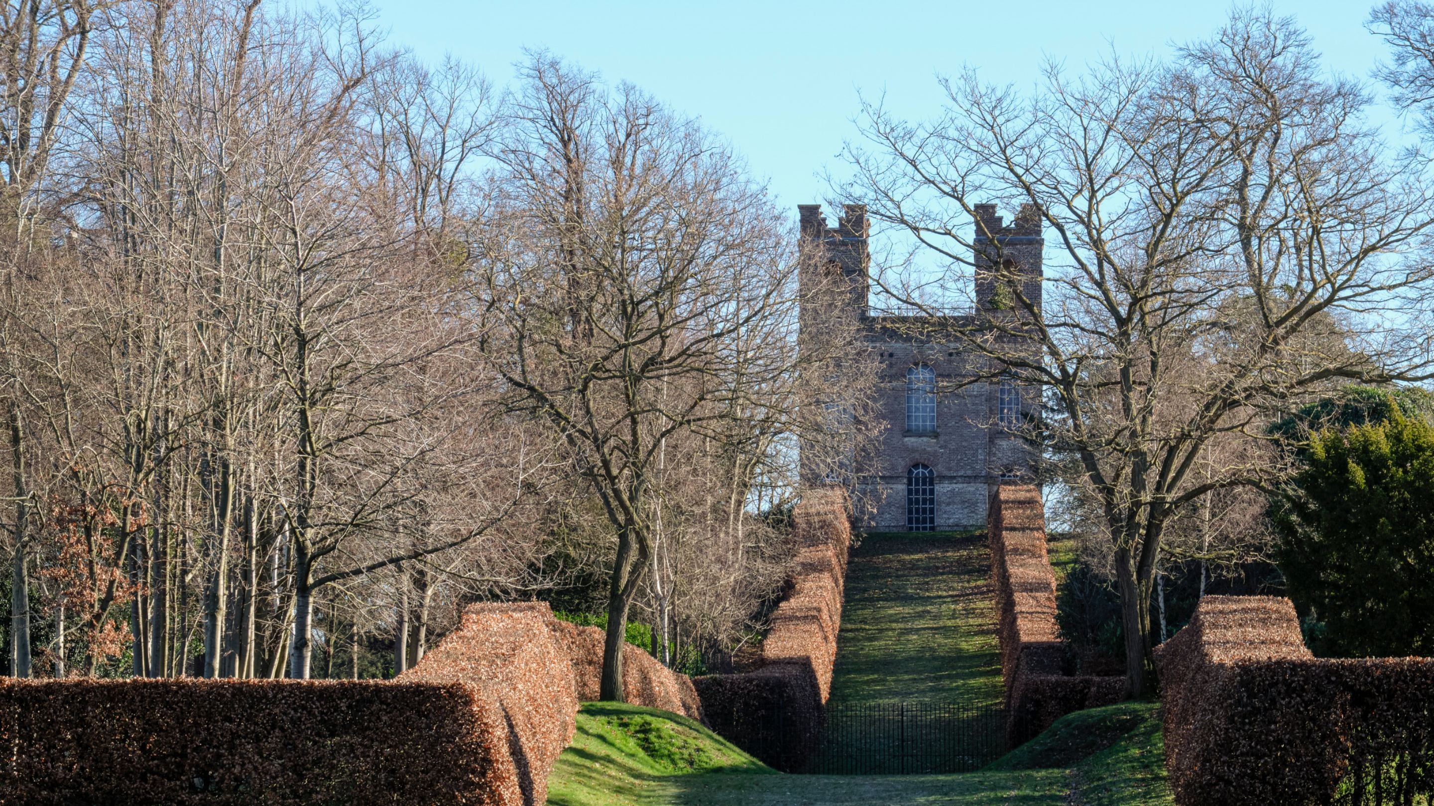 Small building with two turrets with a green hill path leading up to it surrounded by trees