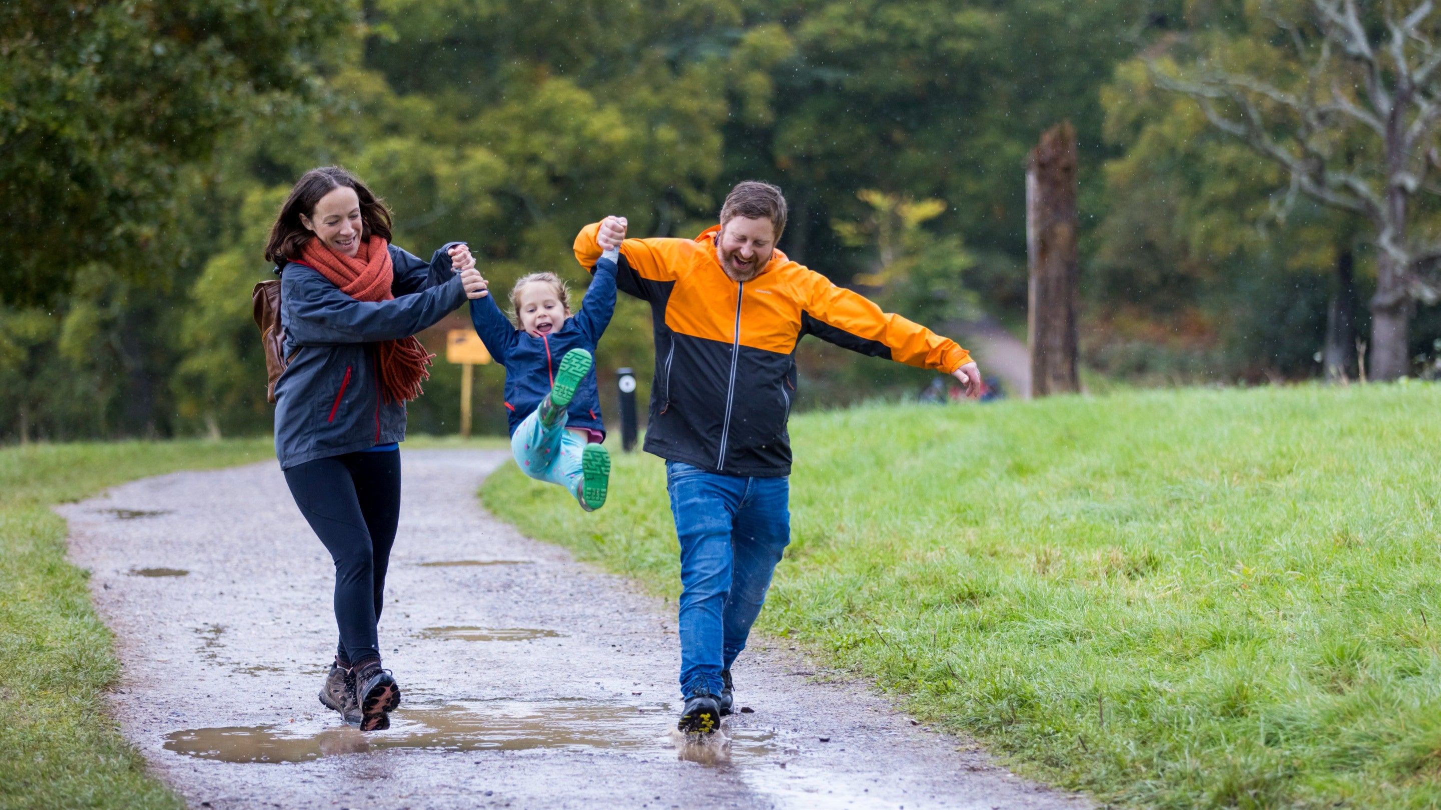 A mother and father holding hands with their child and swinging them in the air, while they all laugh