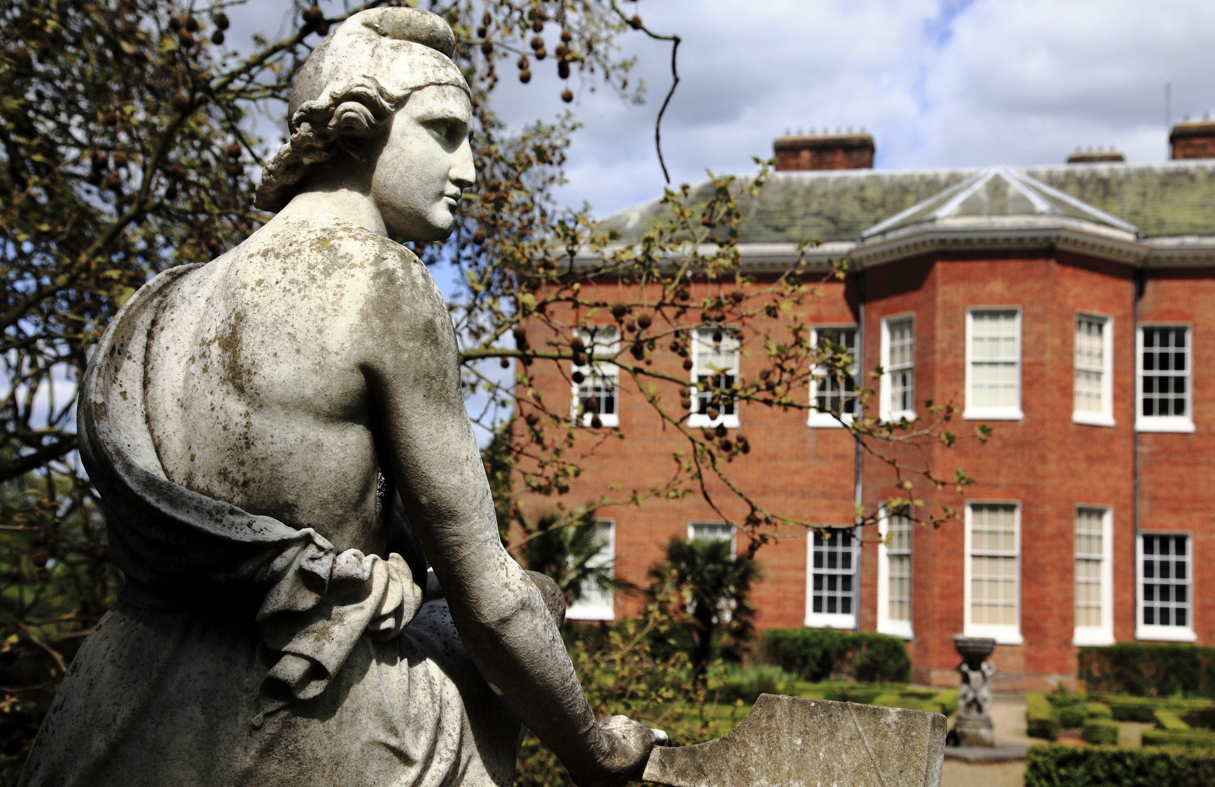 A wistful looking stone statue of "Paris", sitting on a lichen covered plinth in the grounds of Hatchlands Park, Surrey