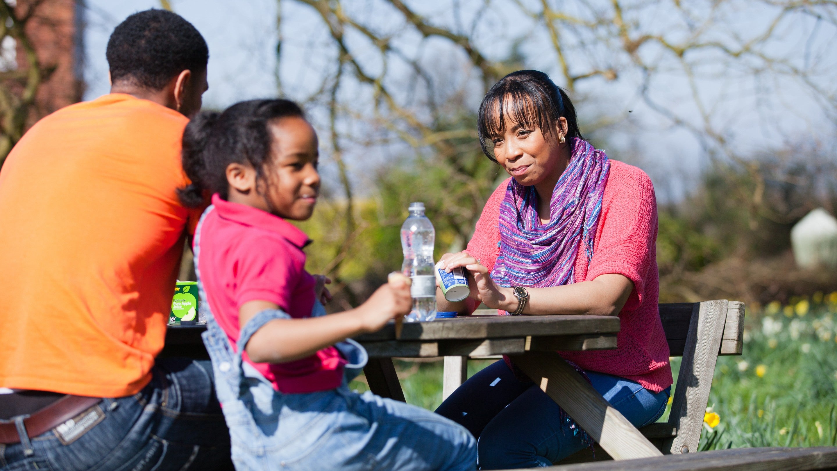 A family enjoying a picnic on a wooden picnic bench, surrounded by daffodils