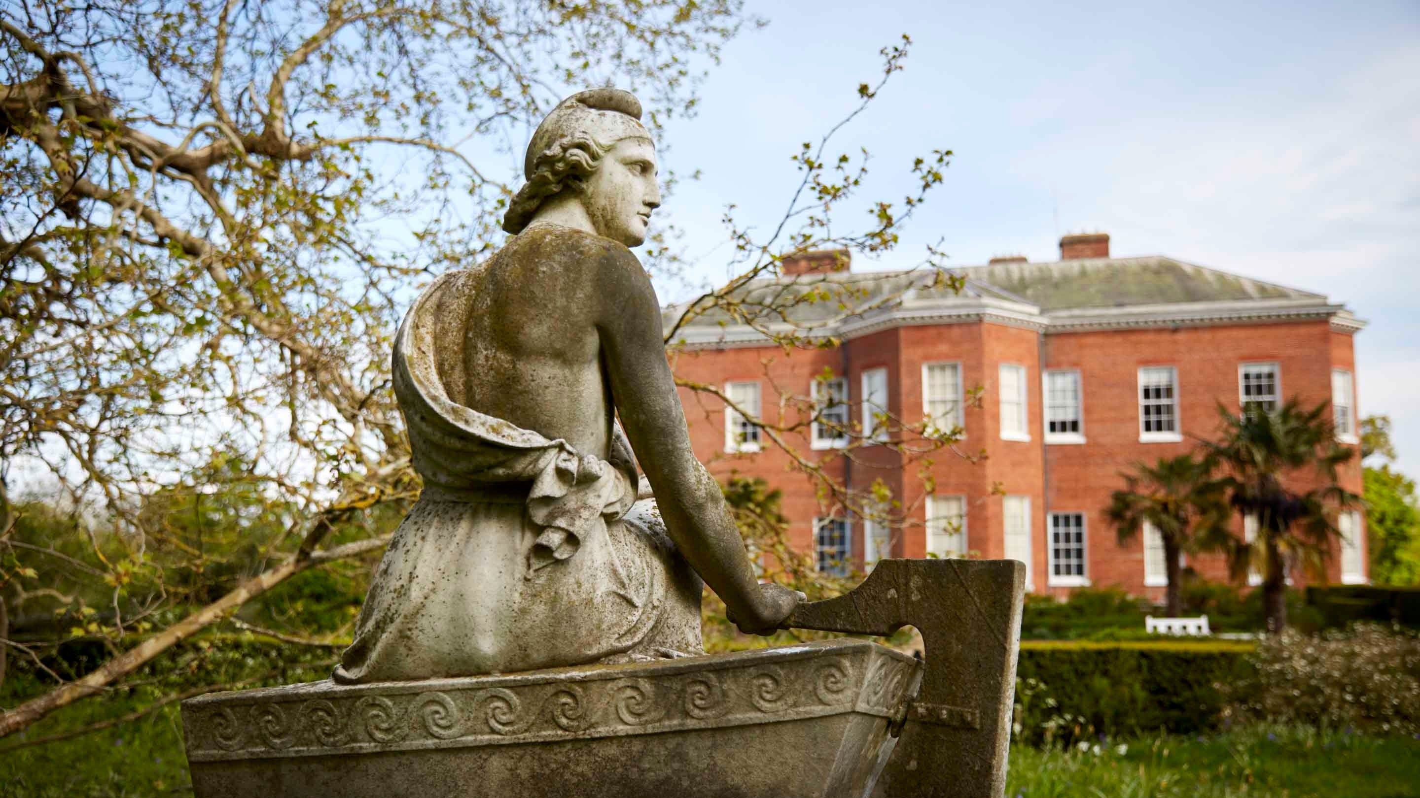 A wistful looking stone statue of "Paris", sitting on a lichen covered plinth in the grounds of Hatchlands Park, Surrey