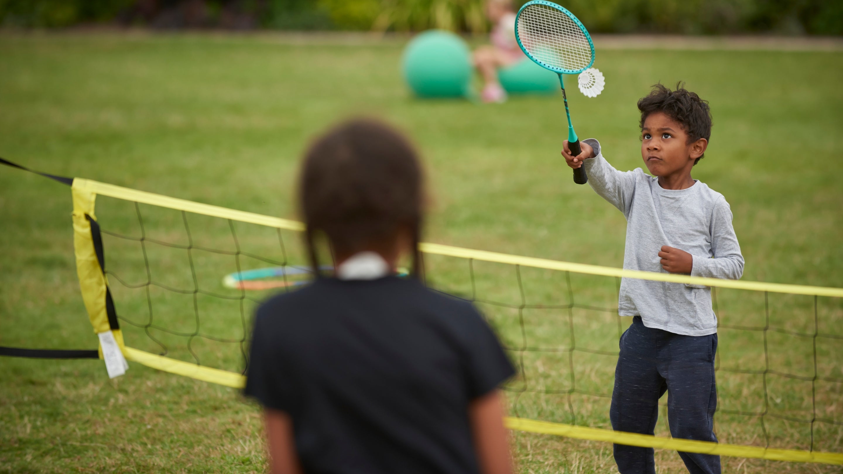 A boy and a girl playing badminton on the lawn at Hatchlands Park