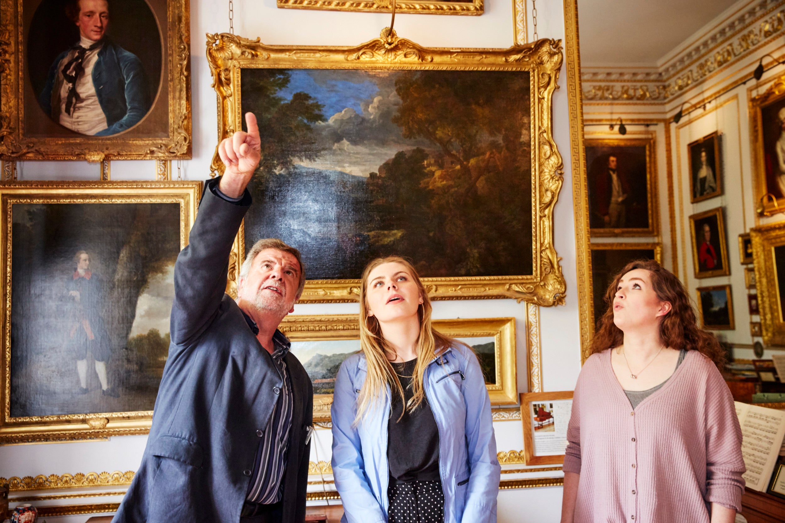 Volunteer pointing at a piece of artwork out of shot with two visitors in the Drawing Room at Hatchlands Park