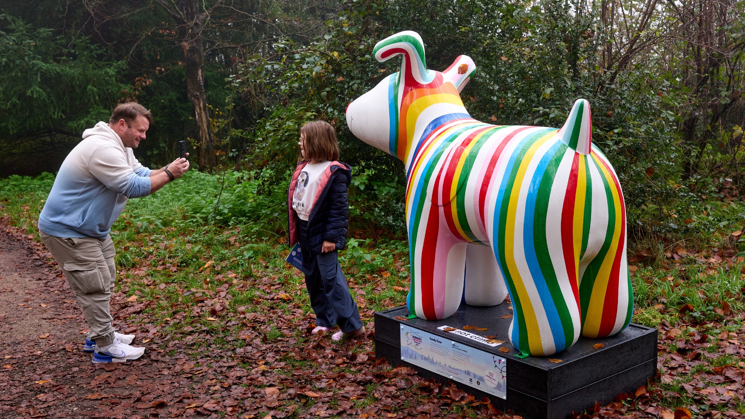 A man taking a picture of a girl in front of colourful striped sculpture of a snowdog.