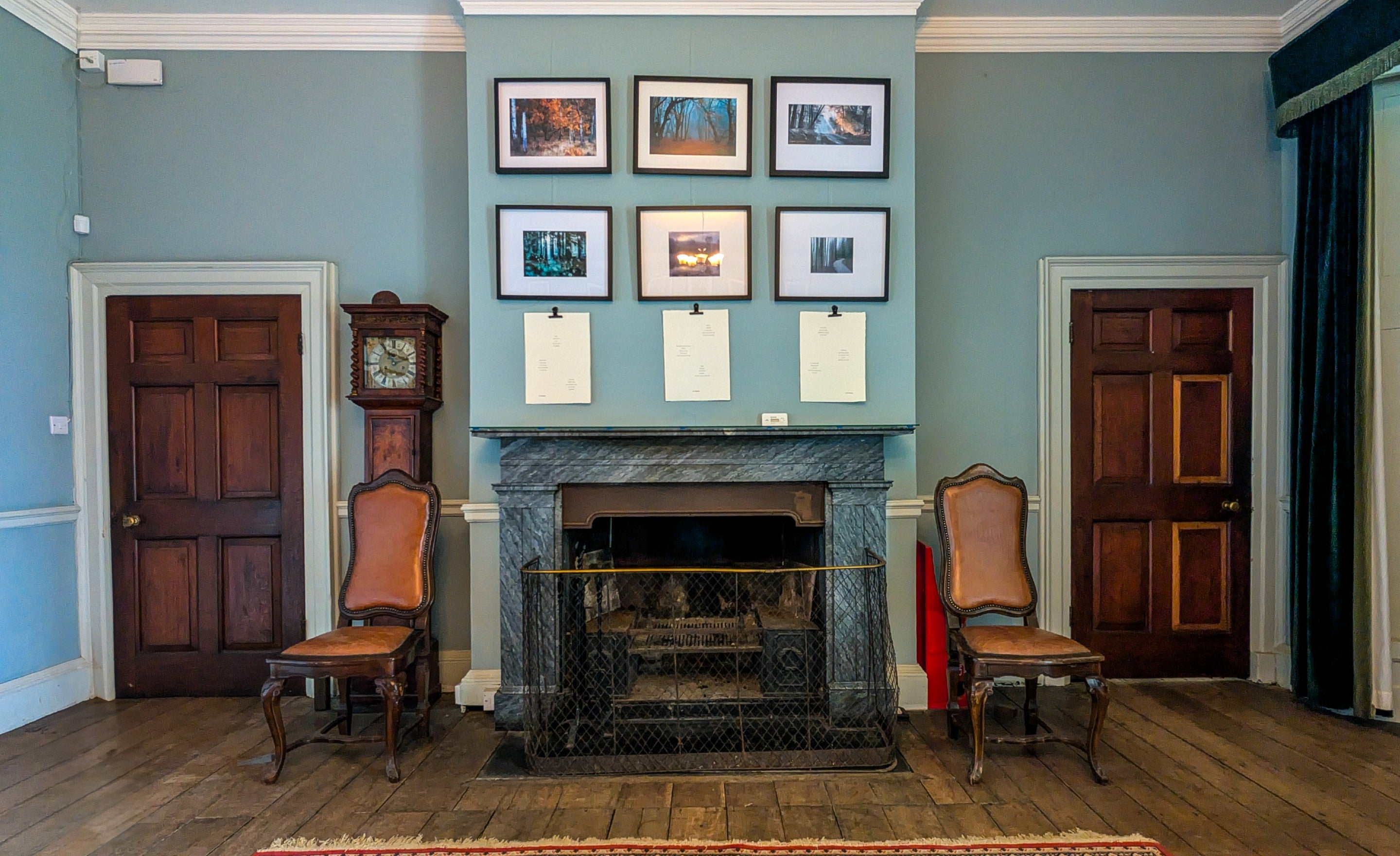 View of framed photographs hanging on the walls in the Terrace Room. The Terrace room has varnished wood floorboards and teal coloured walls.