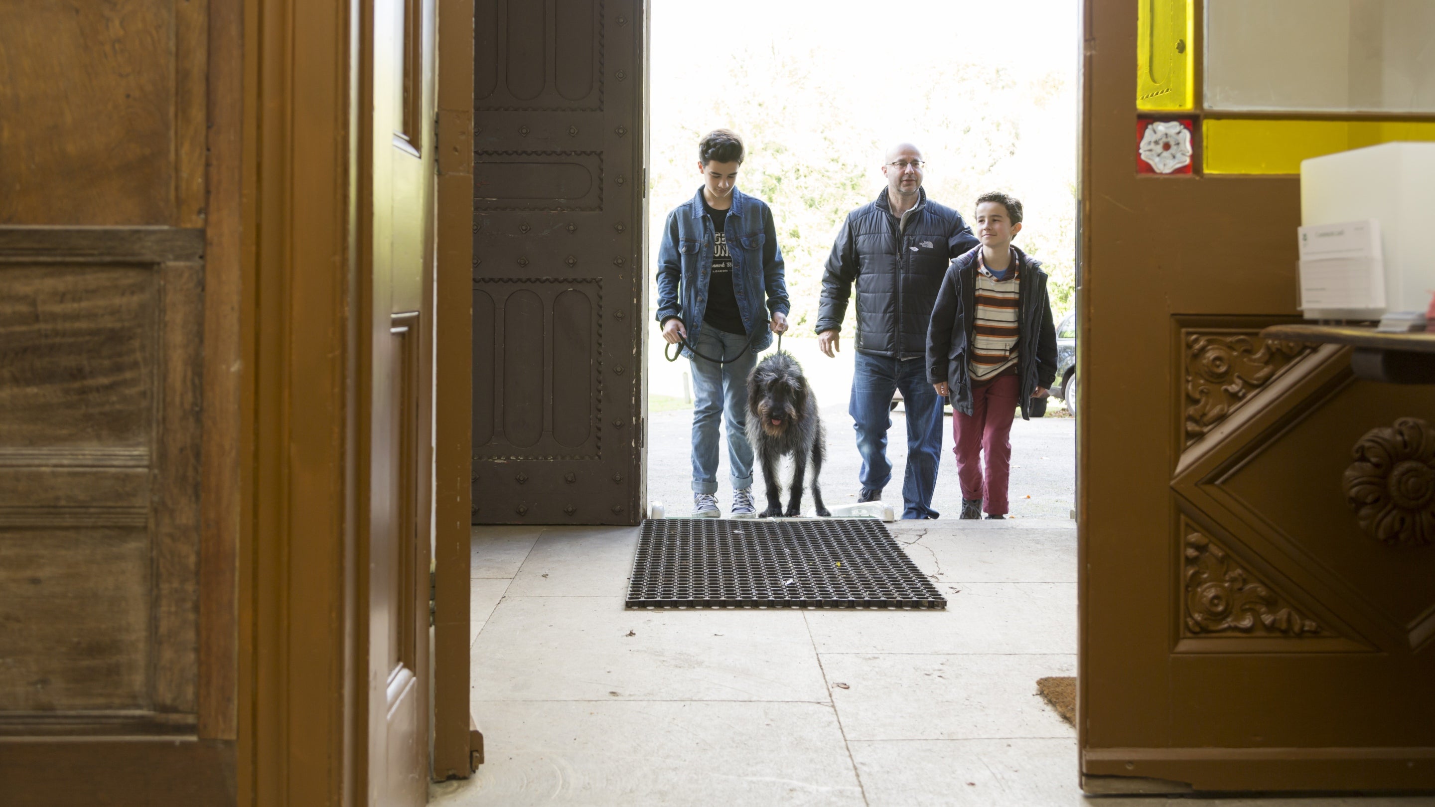 A man, two children and a dog walk up the front steps to enter Leith Hill Place, Surrey. The photo is taken from inside the double doors inside