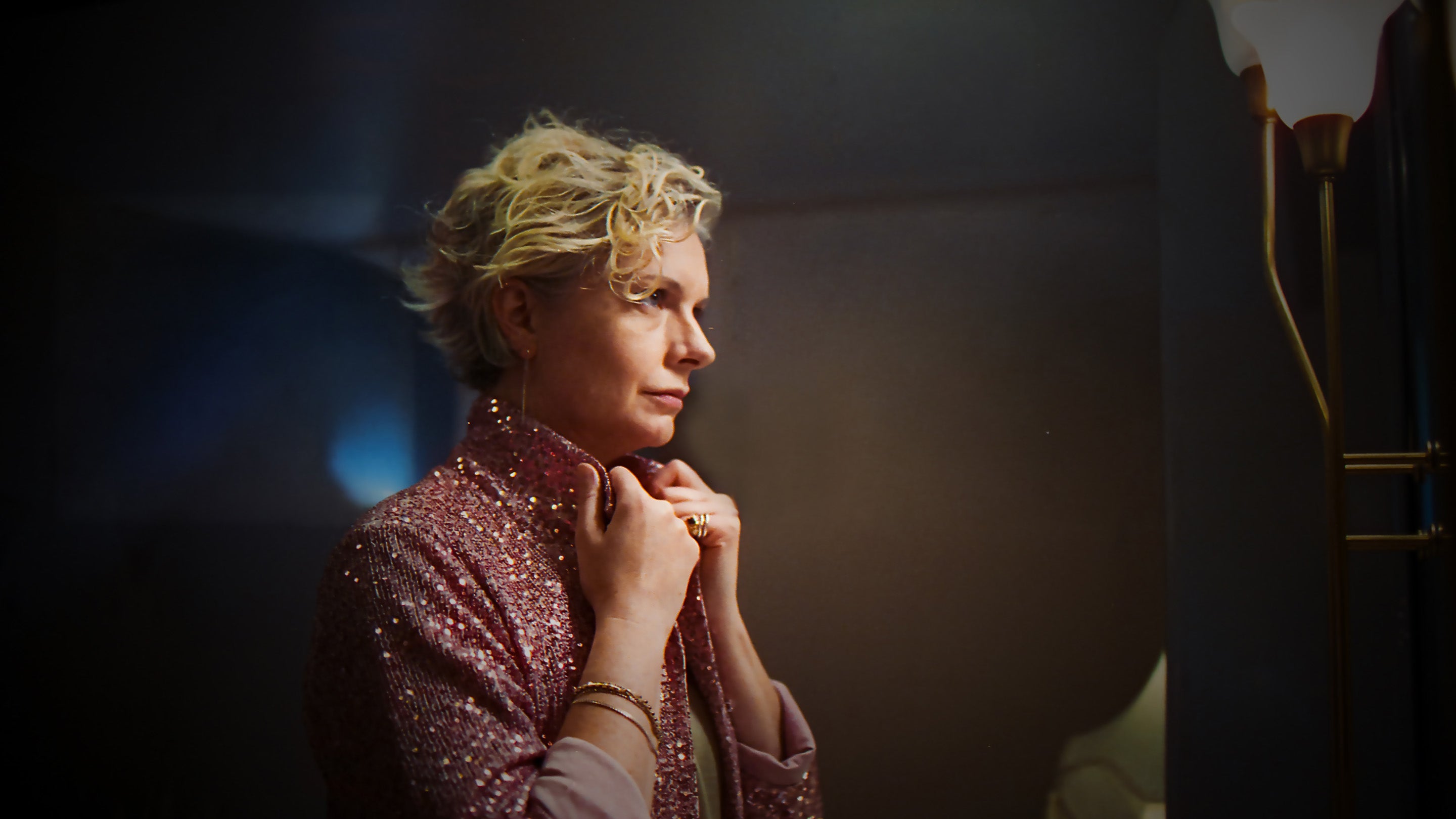Profile of a woman with blonde hair in a sparkling top looking in the mirror