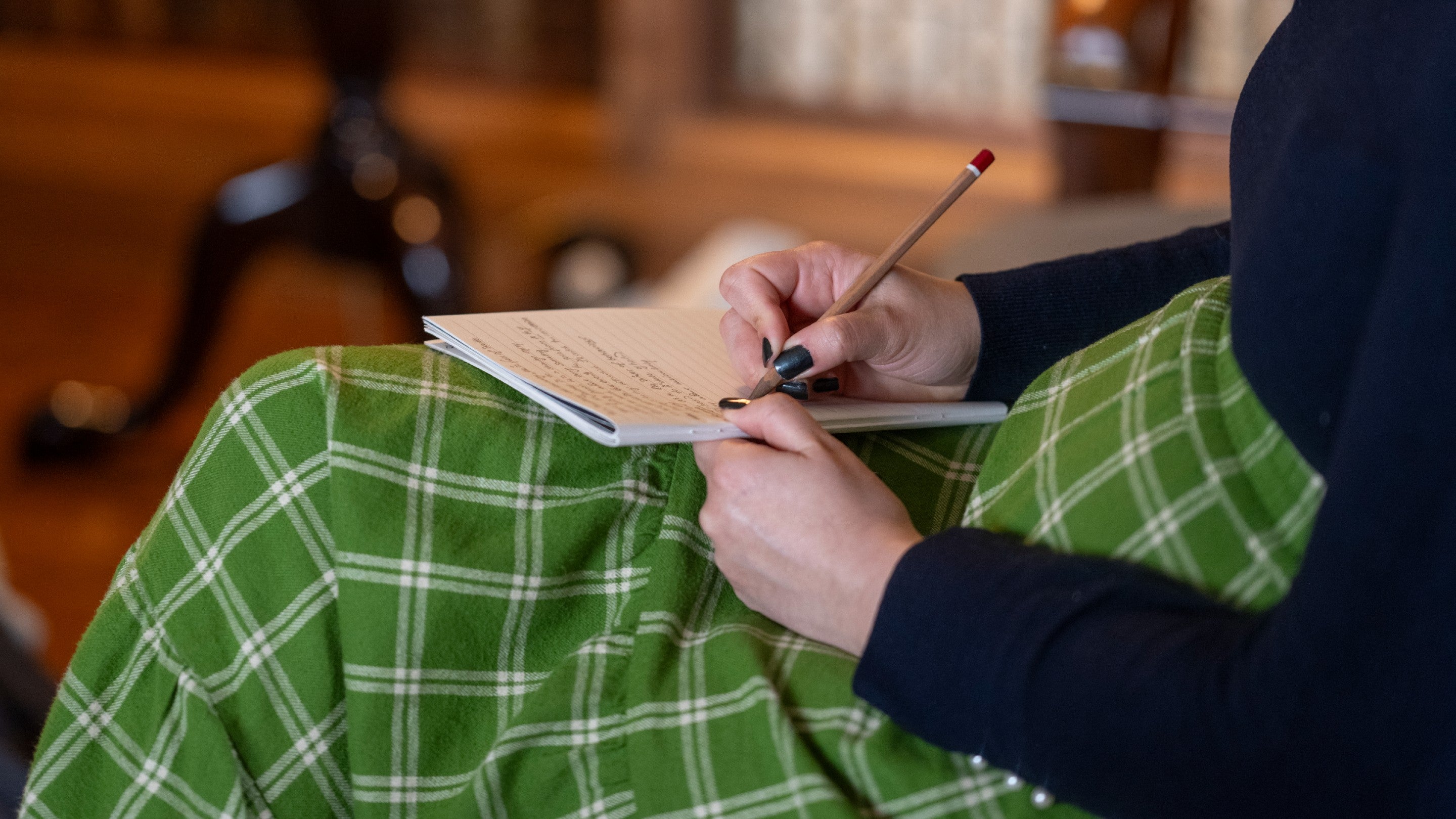 Woman wearing a green and white checked skirt, writing on a pad resting on her knee