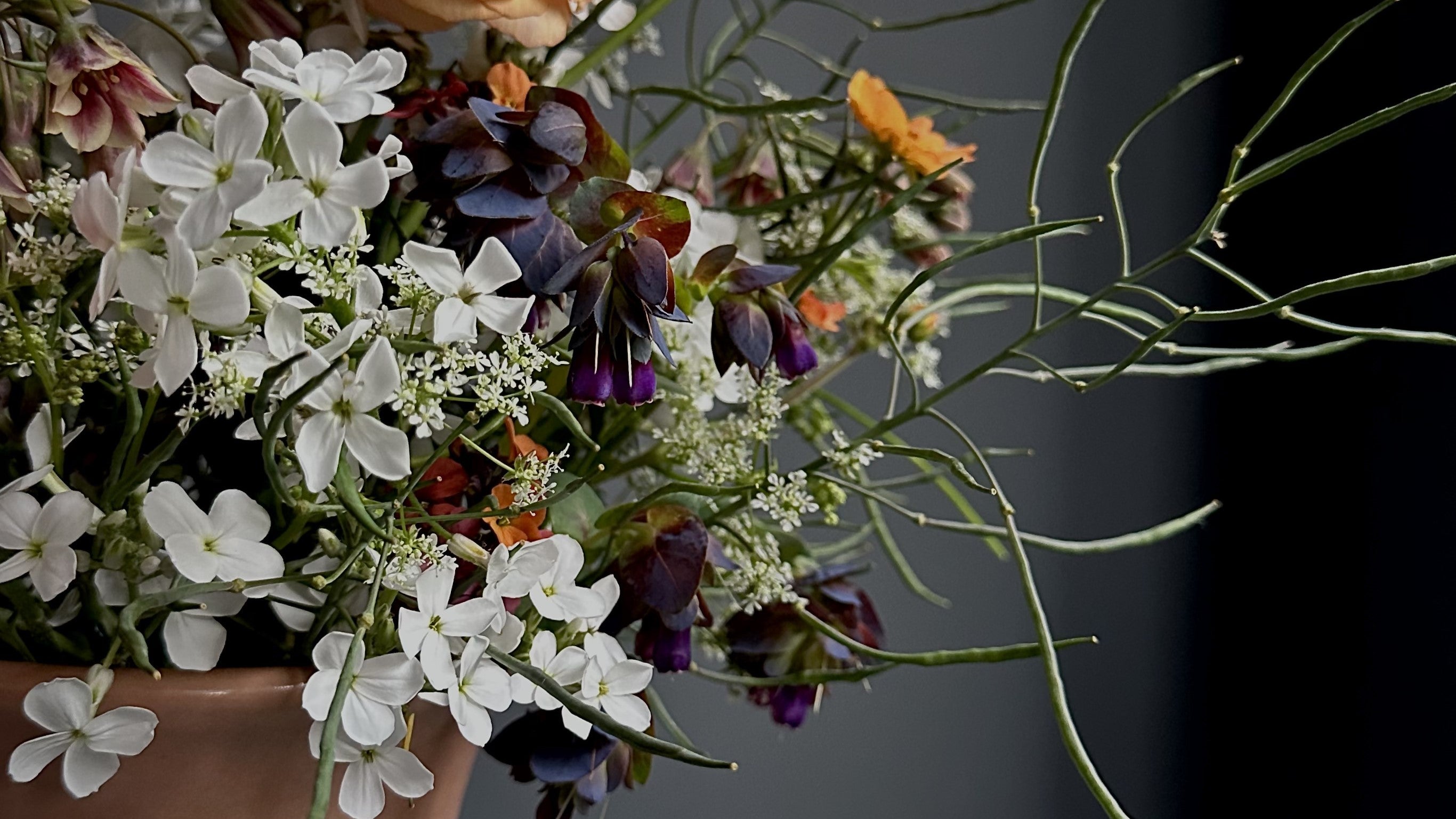 A multicoloured floral arrangement with foliage in a peach coloured ceramic bowl